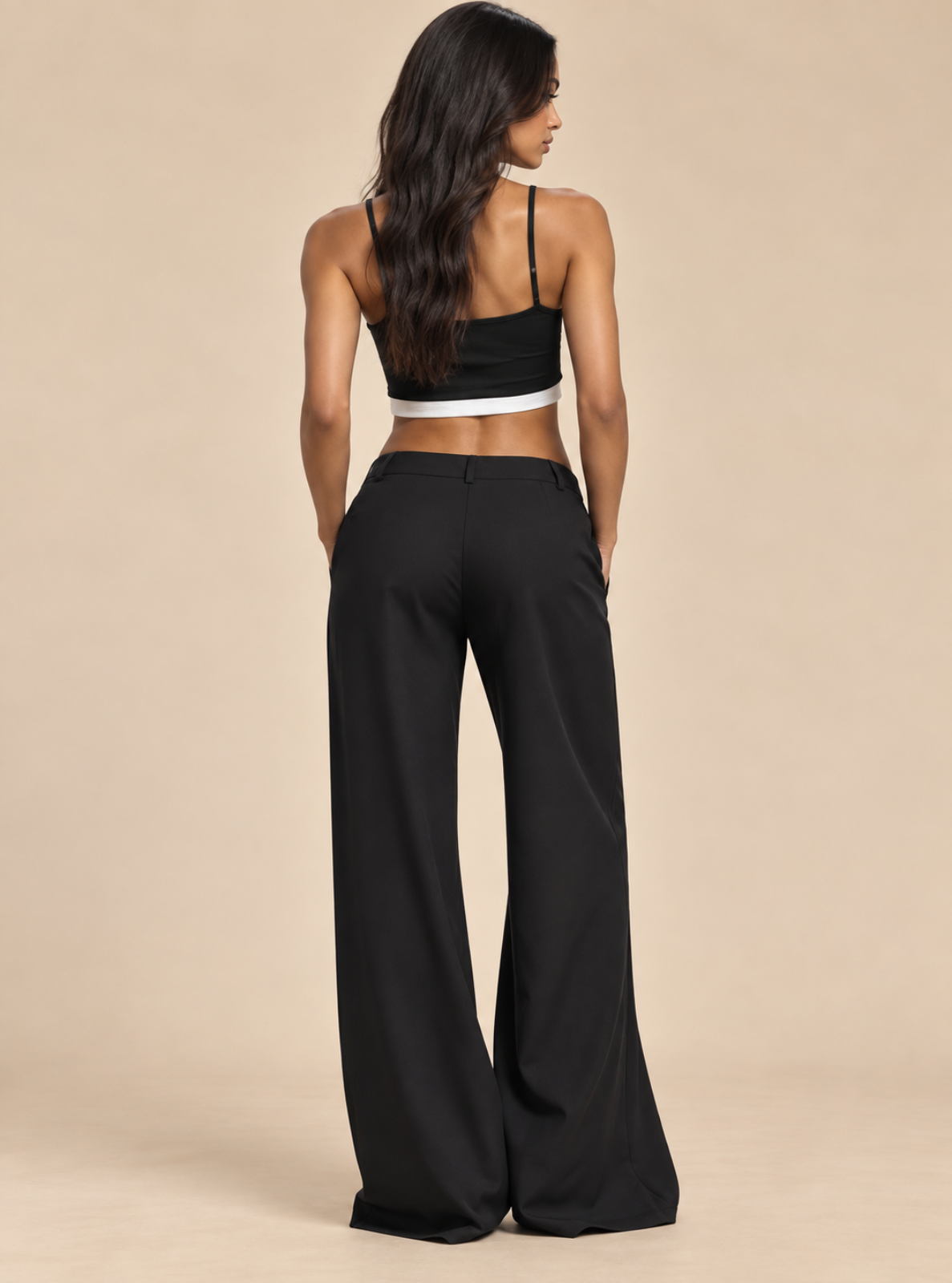 A woman shown from the back wearing black wide-leg pants and a black halter crop top with a white band detail, standing against a solid beige studio background.