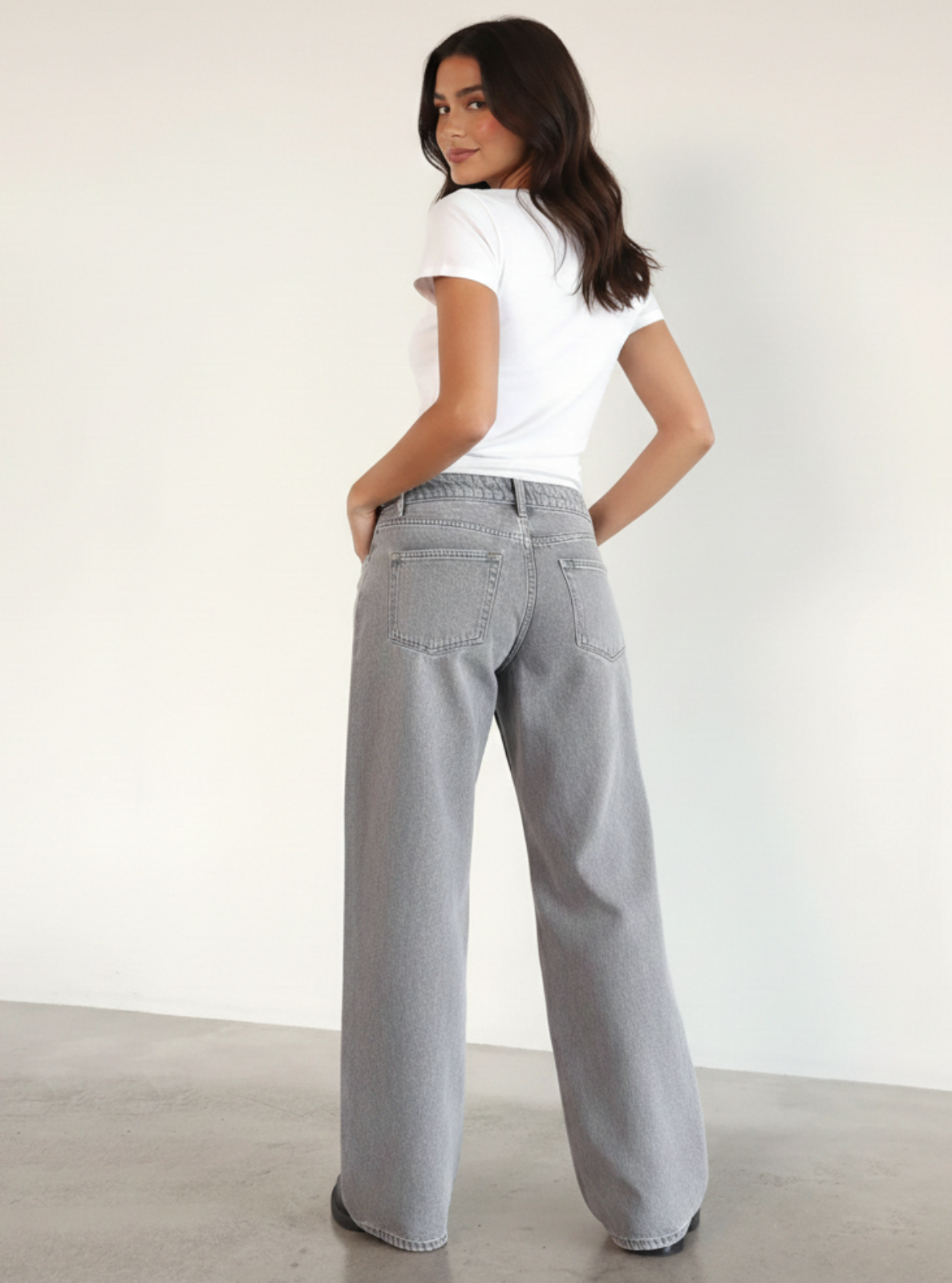 Woman wearing a white t-shirt and gray wide-leg jeans against a plain background