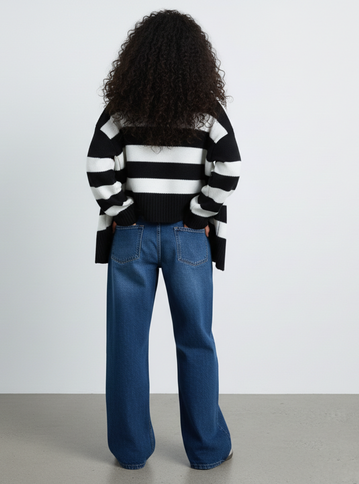 Person wearing a black and white striped sweater and blue jeans from behind on a plain background