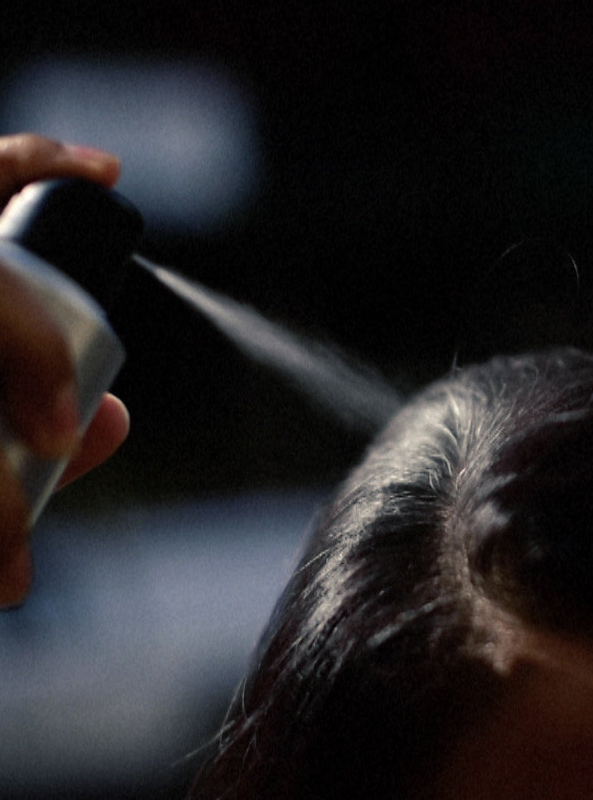 Person using a hair dryer on their hair with a dark background