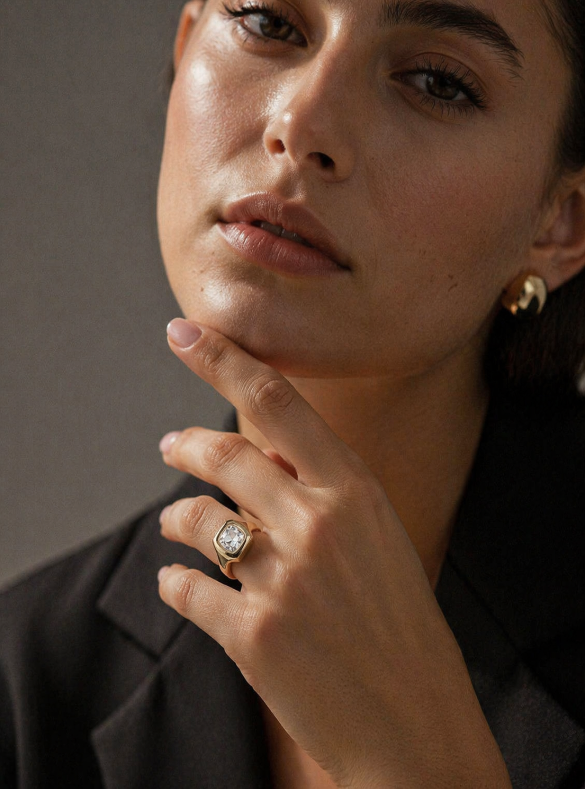 Close-up of a woman wearing a gold ring with a diamond on her finger, against a neutral background.