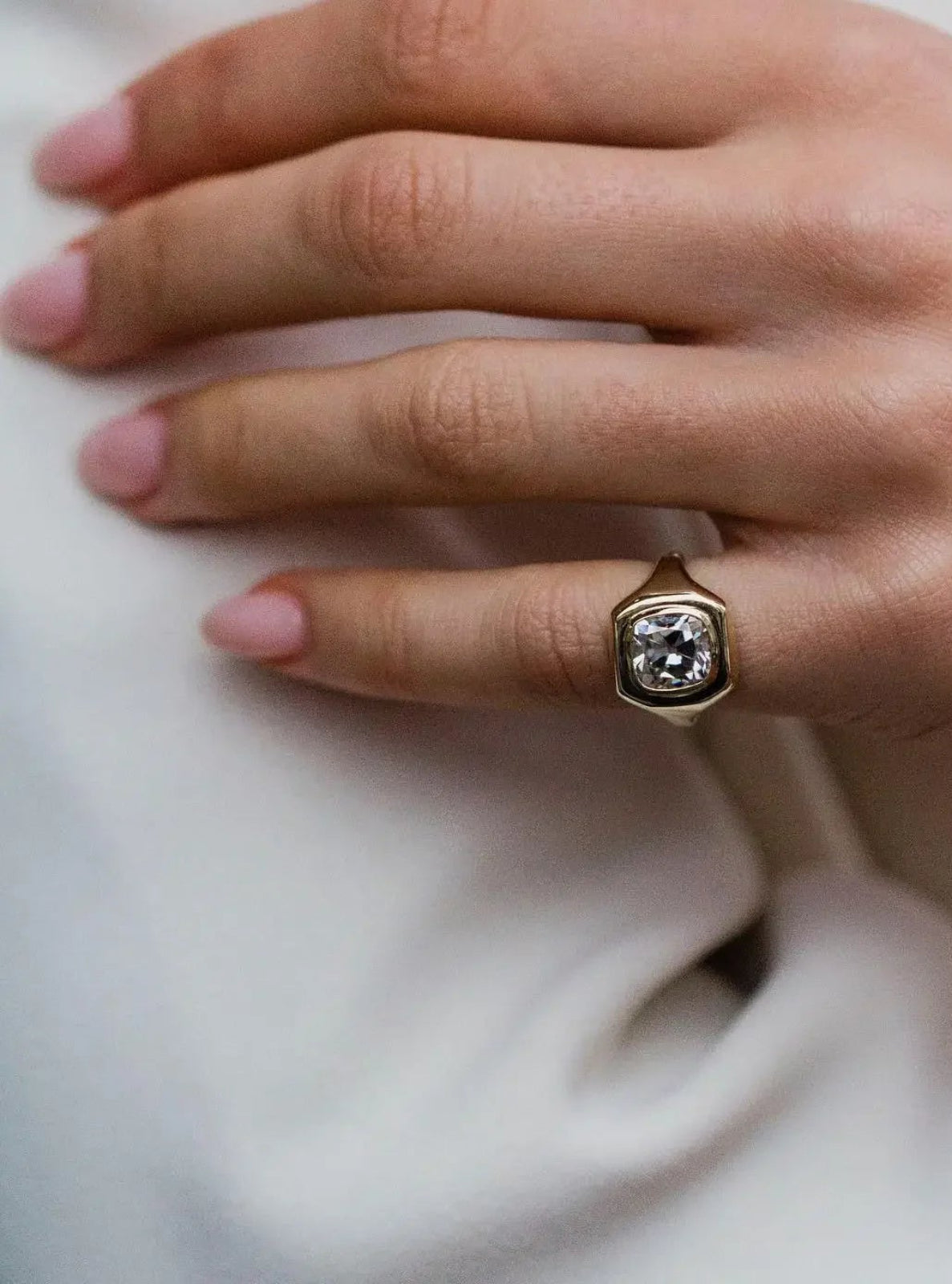 Close-up of a hand wearing a gold ring with a diamond on a white background