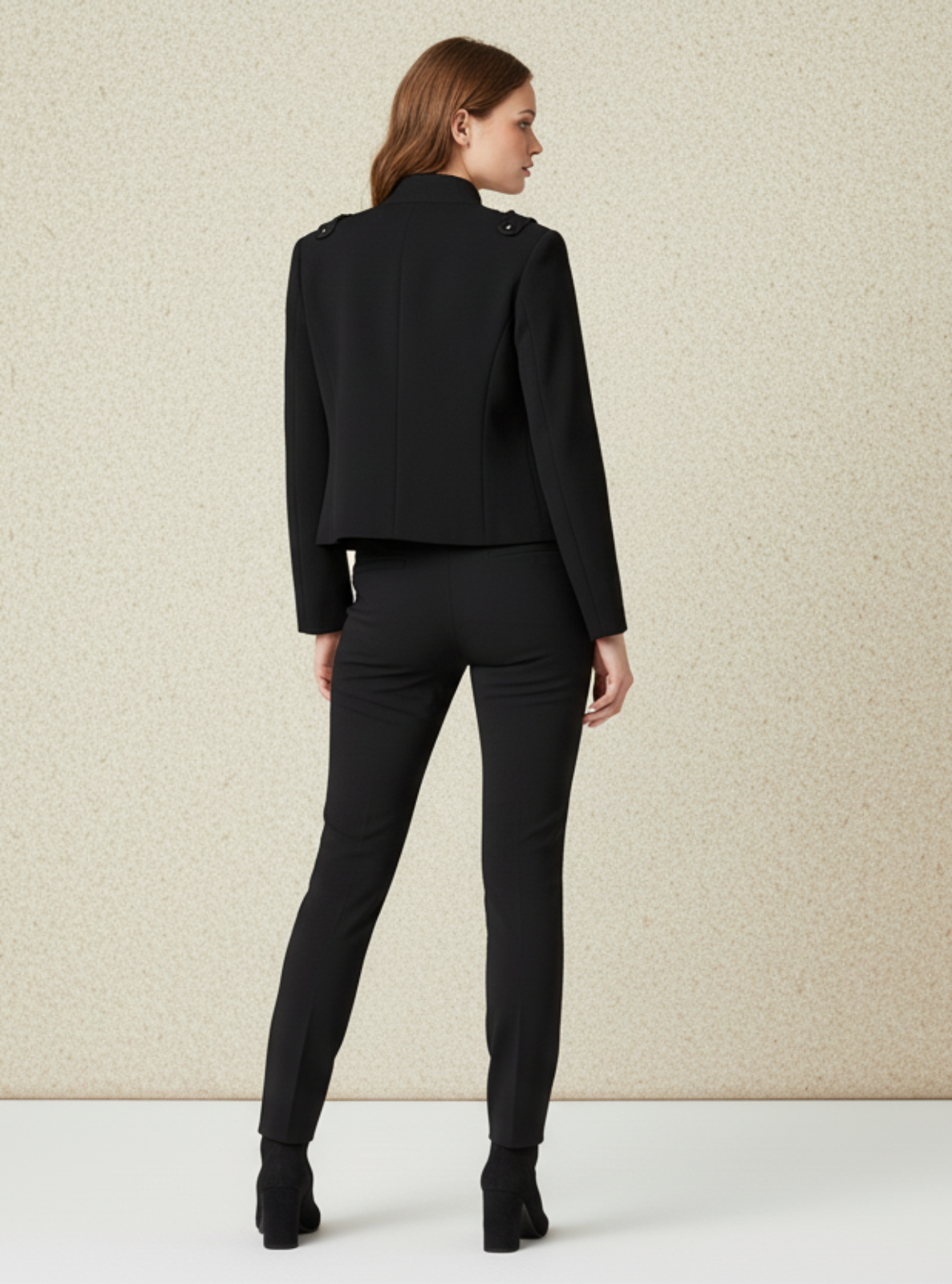 Woman wearing a black suit standing against a beige wall.
