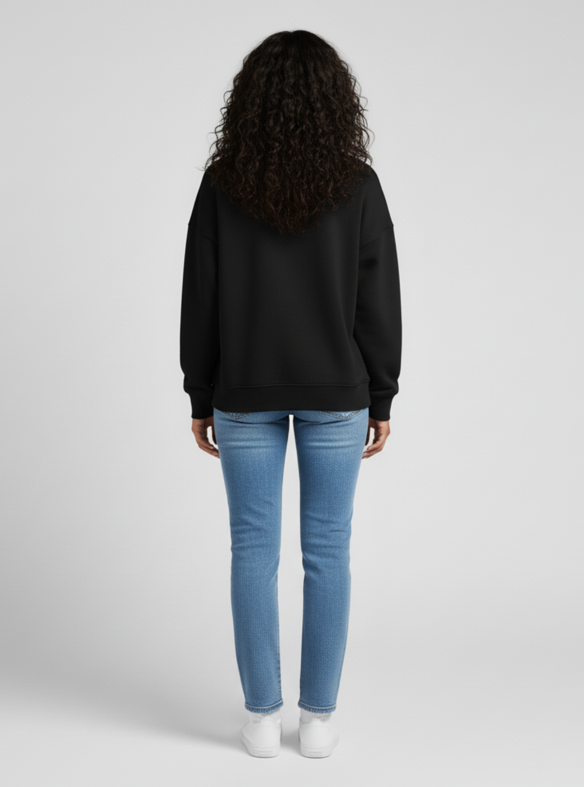 Person wearing a black hoodie and blue jeans on a white background