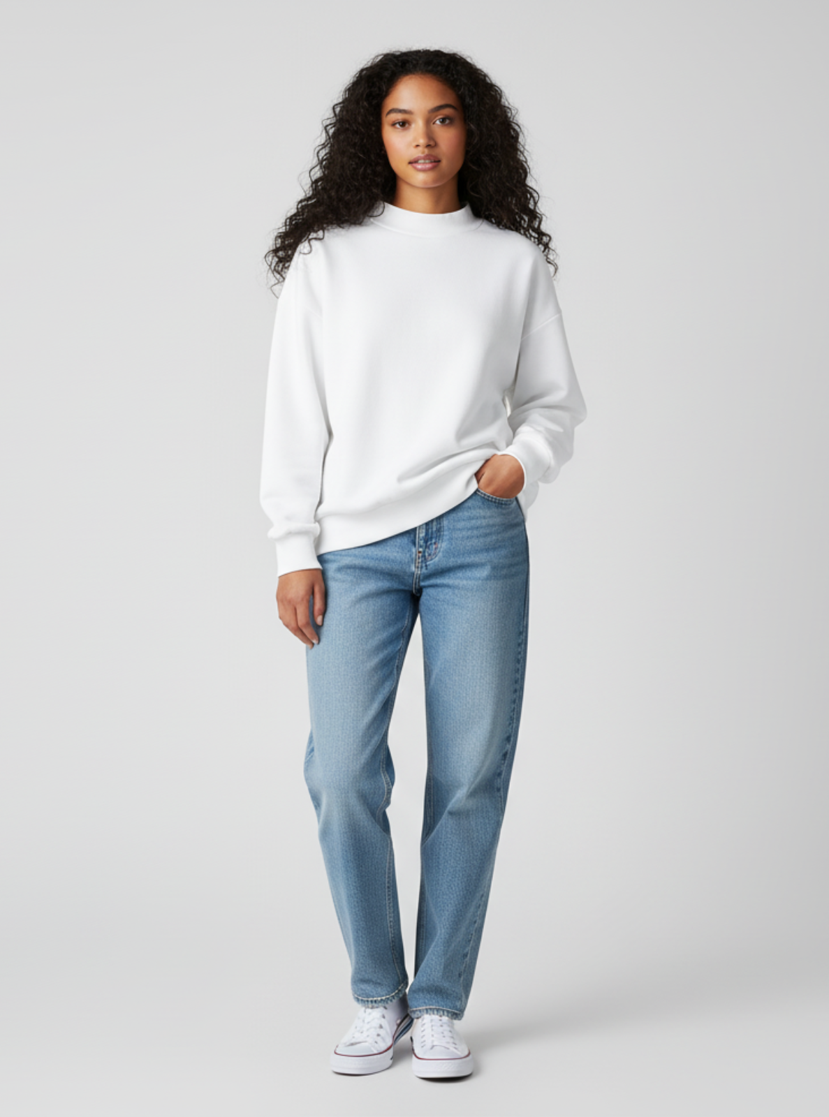 Woman wearing a white sweater and light blue jeans on a plain background