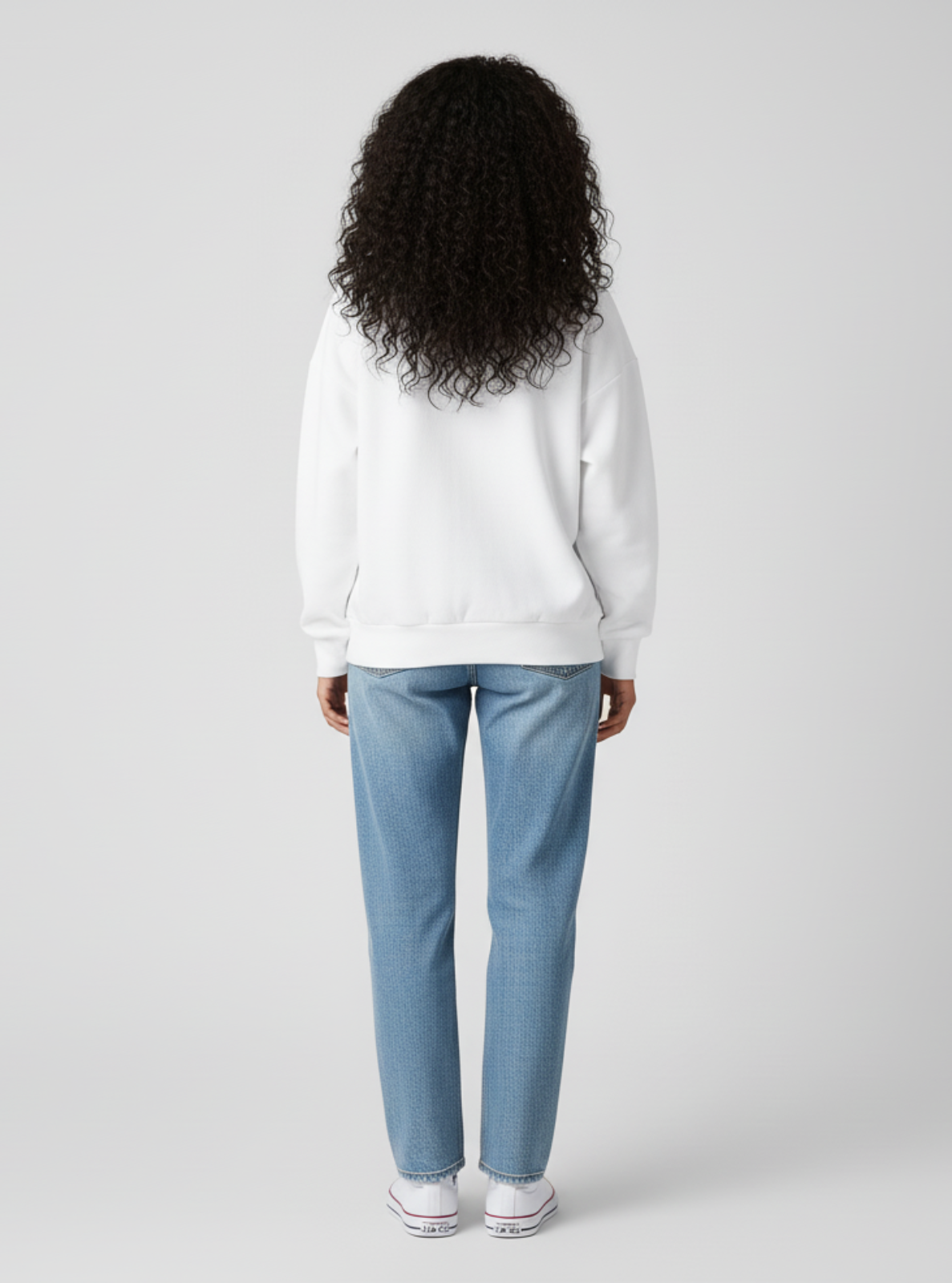Person wearing a white sweatshirt and light blue jeans on a plain background