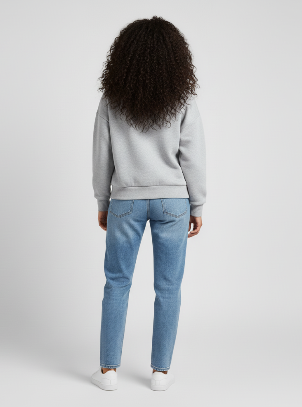 Person wearing a light gray sweatshirt and blue jeans on a white background