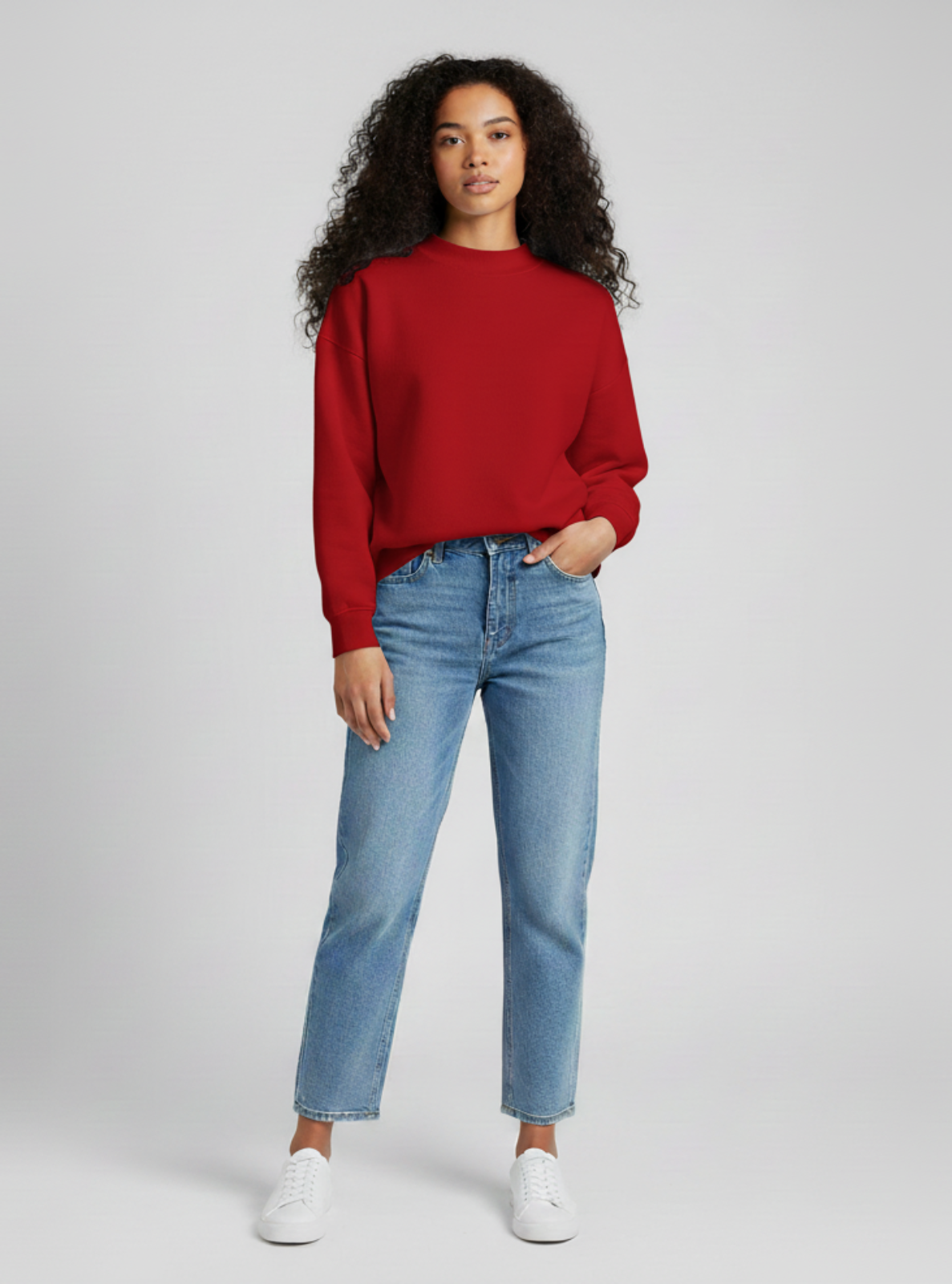 Woman wearing a red sweater and blue jeans on a gray background