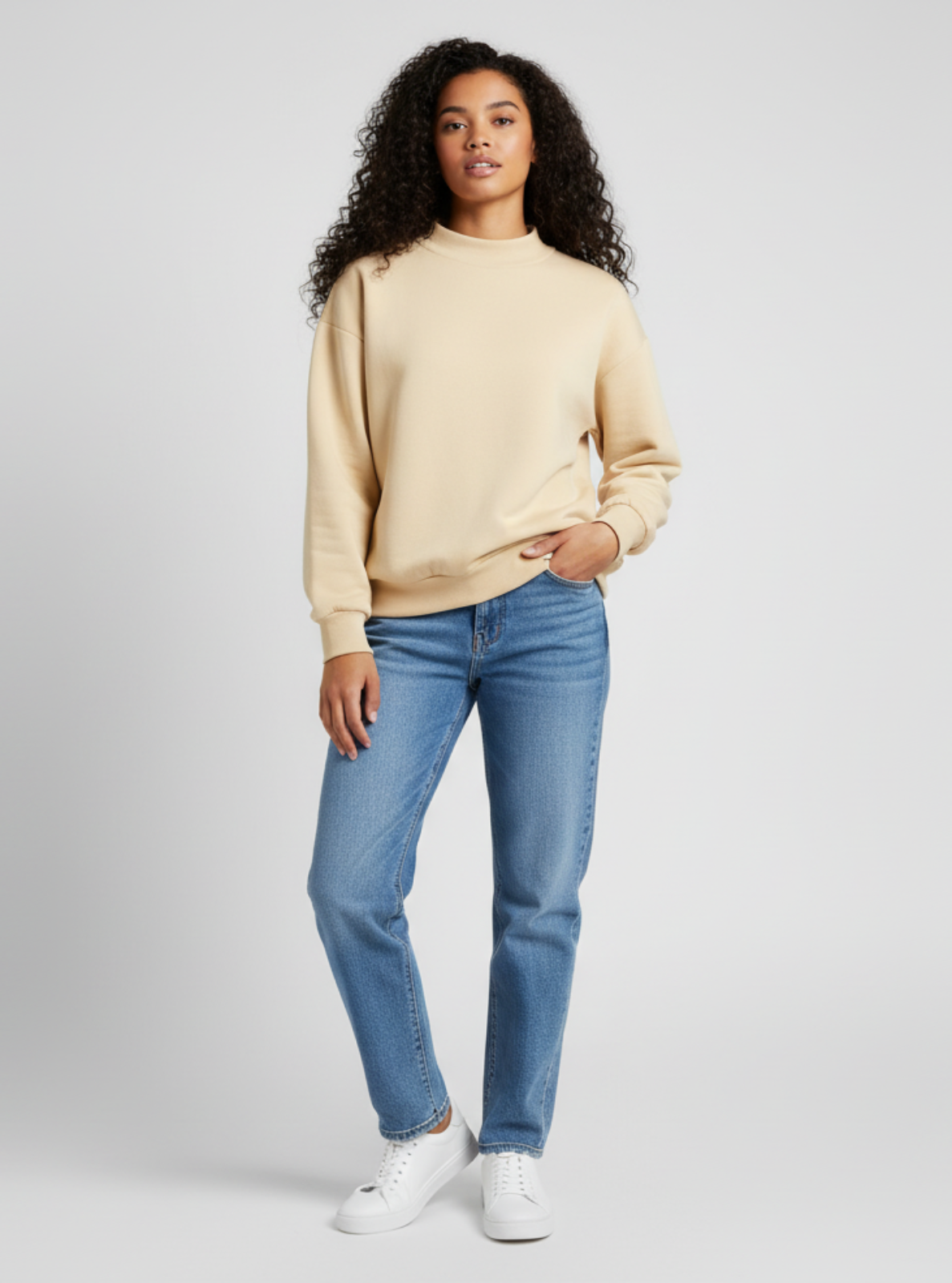 Woman wearing a beige sweater and blue jeans on a gray background