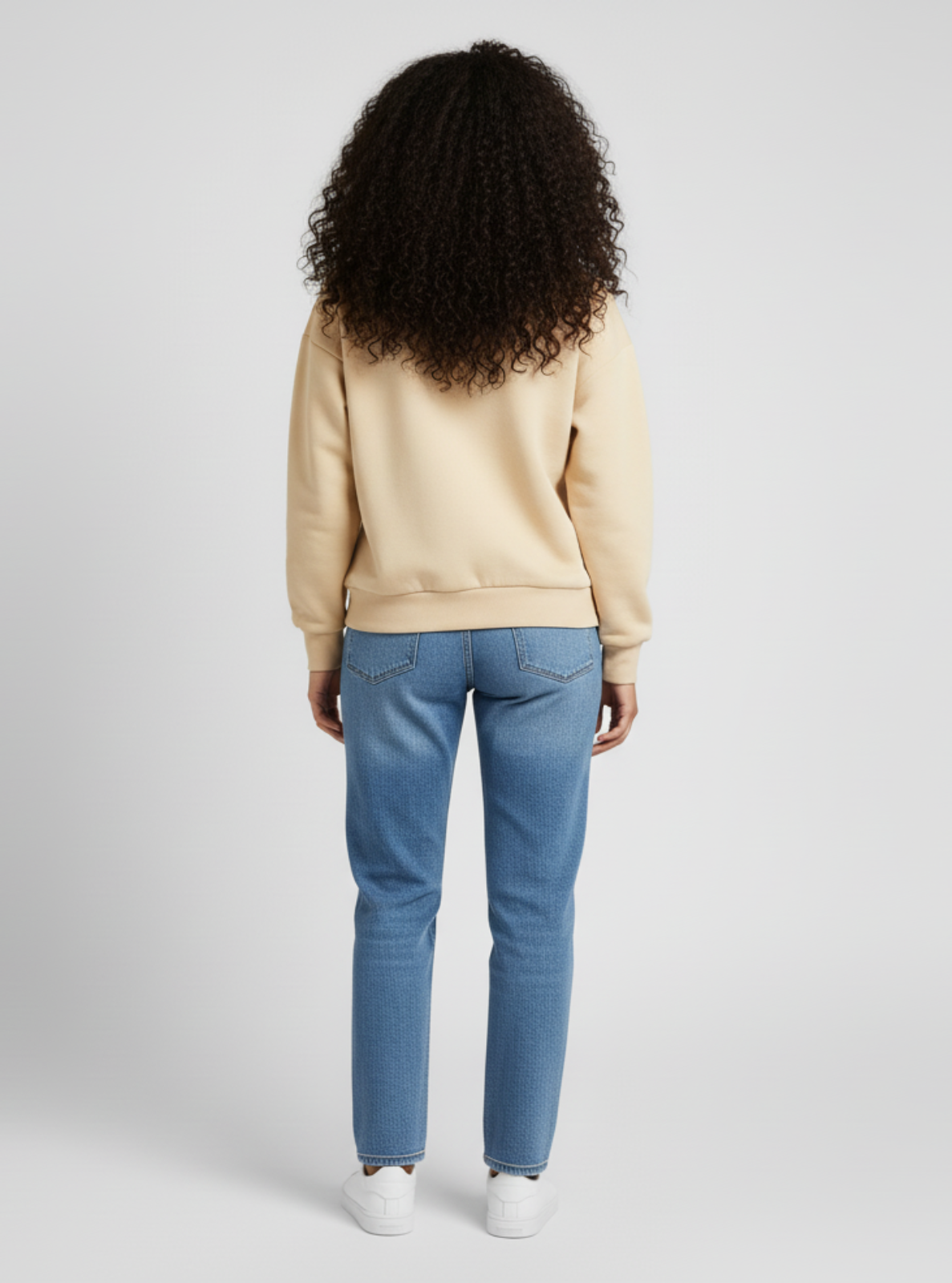 Person wearing a beige sweatshirt and blue jeans on a white background
