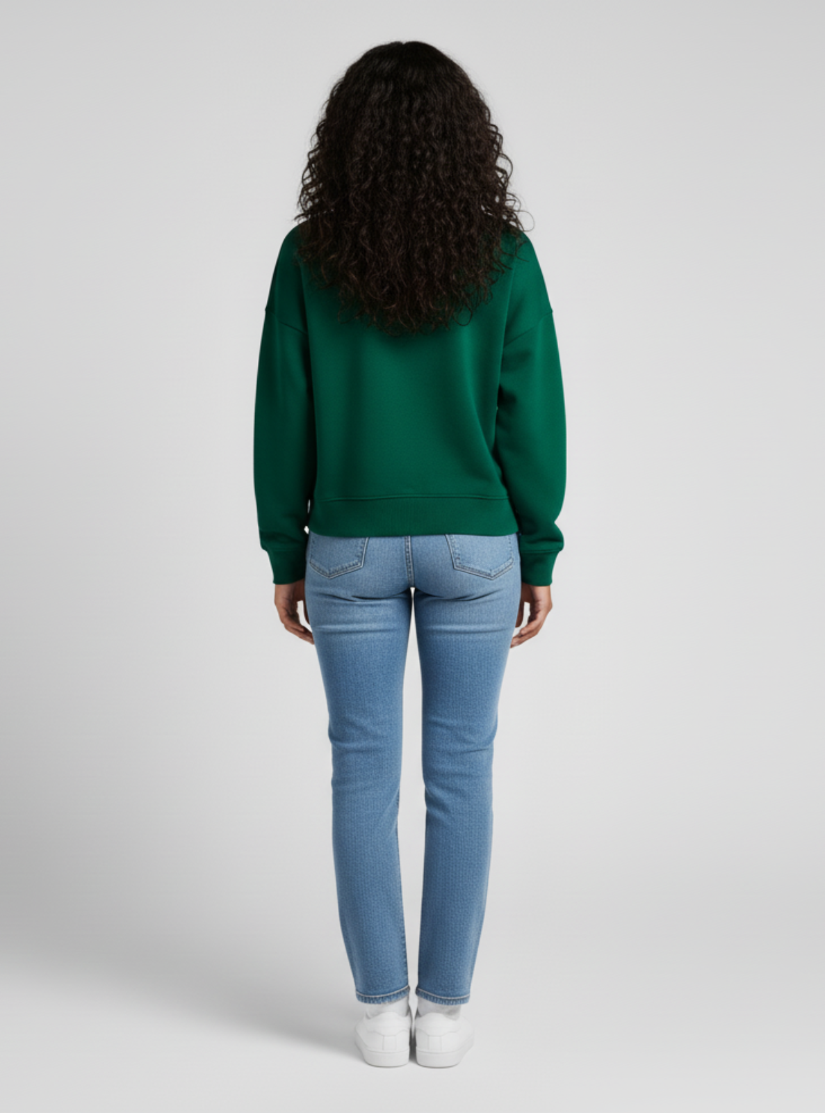 Person wearing a green sweater and blue jeans on a white background