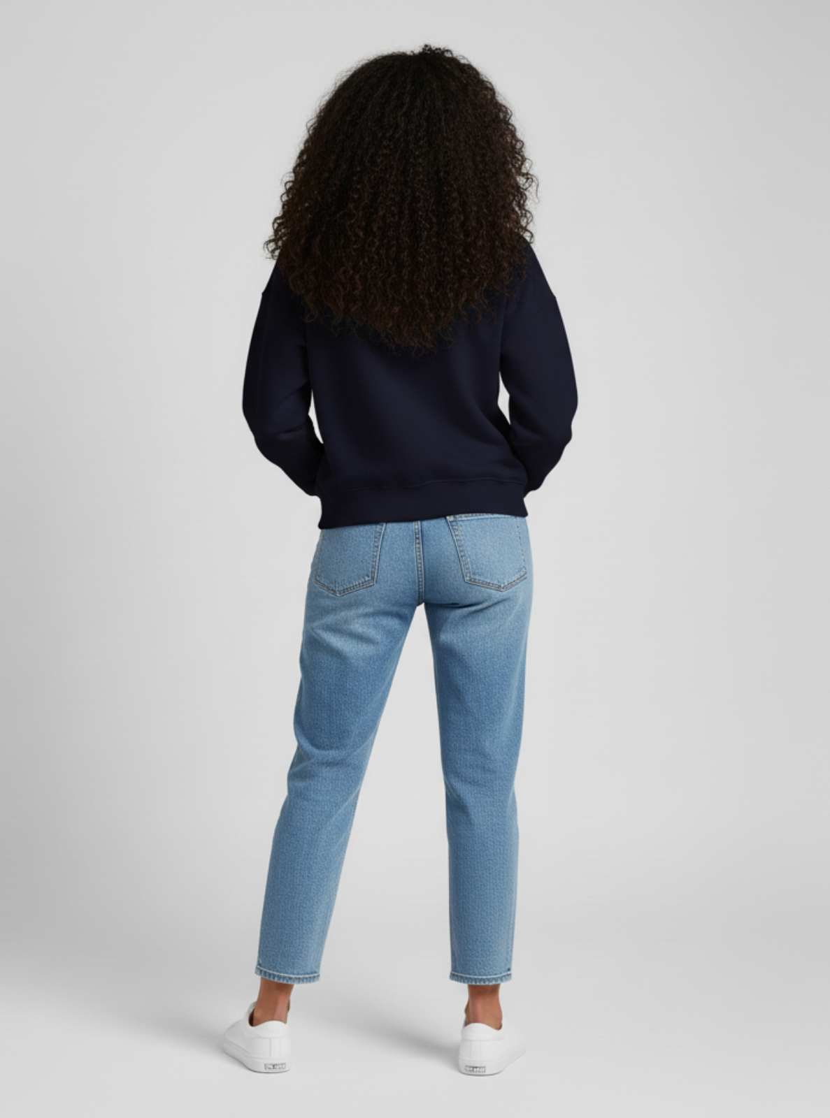Person wearing a navy sweater and light blue jeans on a white background