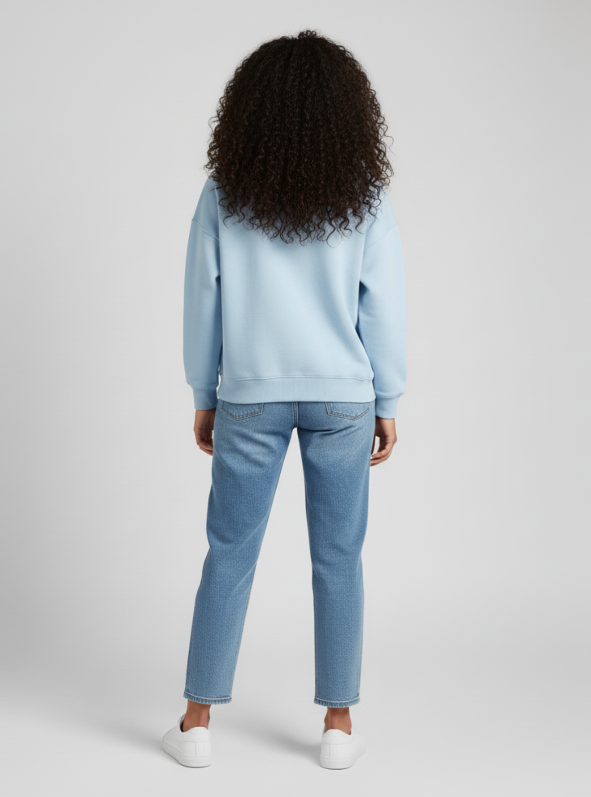 Person wearing a light blue sweatshirt and jeans on a plain background