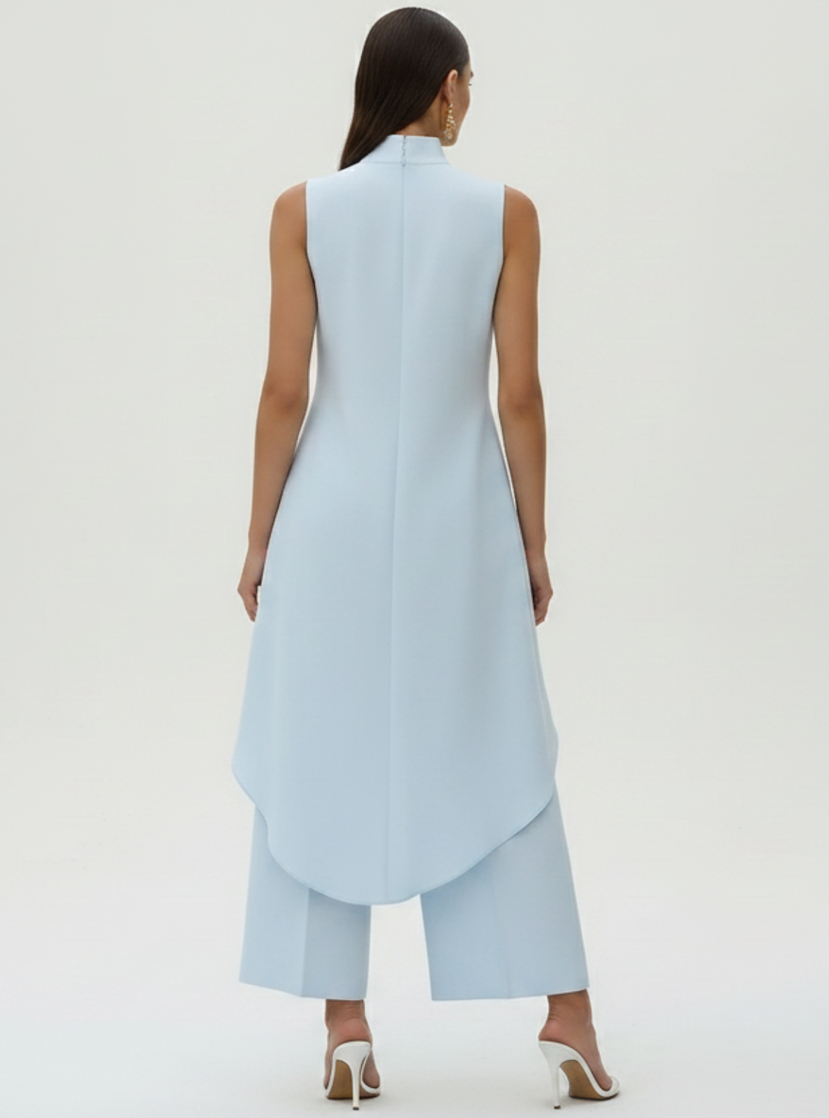Woman wearing a light blue sleeveless top and pants against a white background