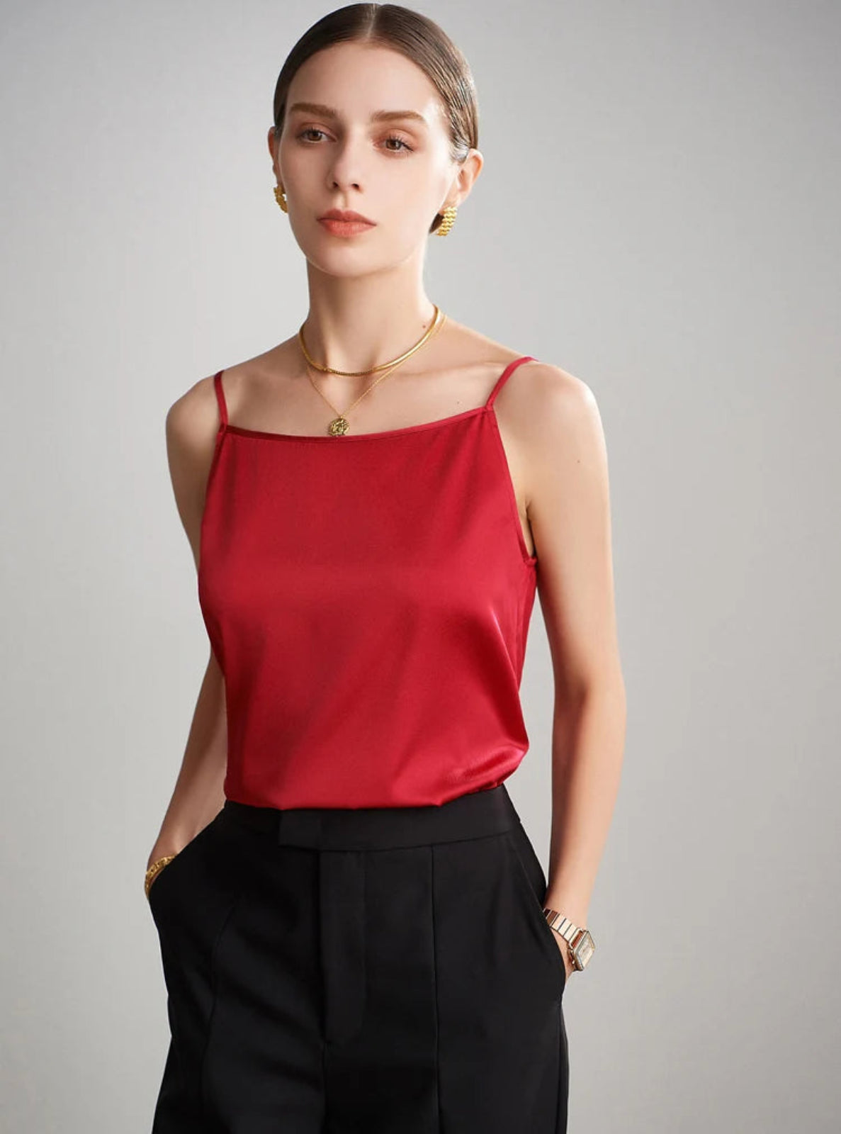 Woman wearing a red top and black pants against a gray background
