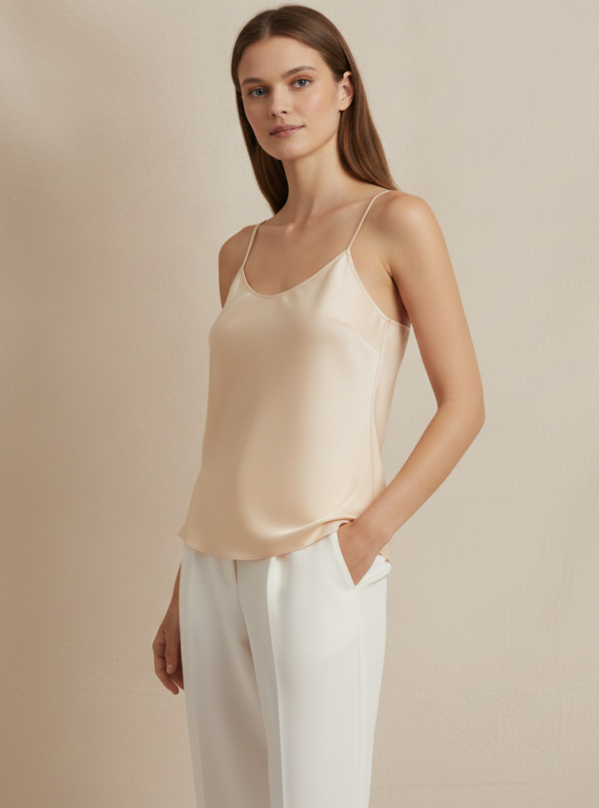 Woman wearing a beige satin camisole and white pants against a beige background