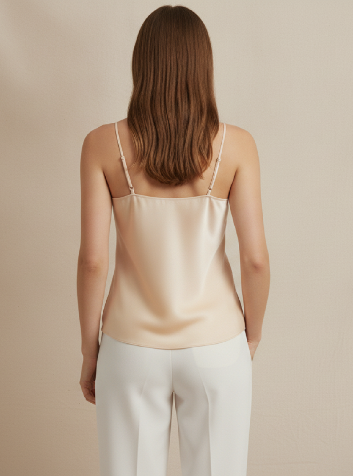 Woman wearing a beige satin camisole and white pants against a beige background