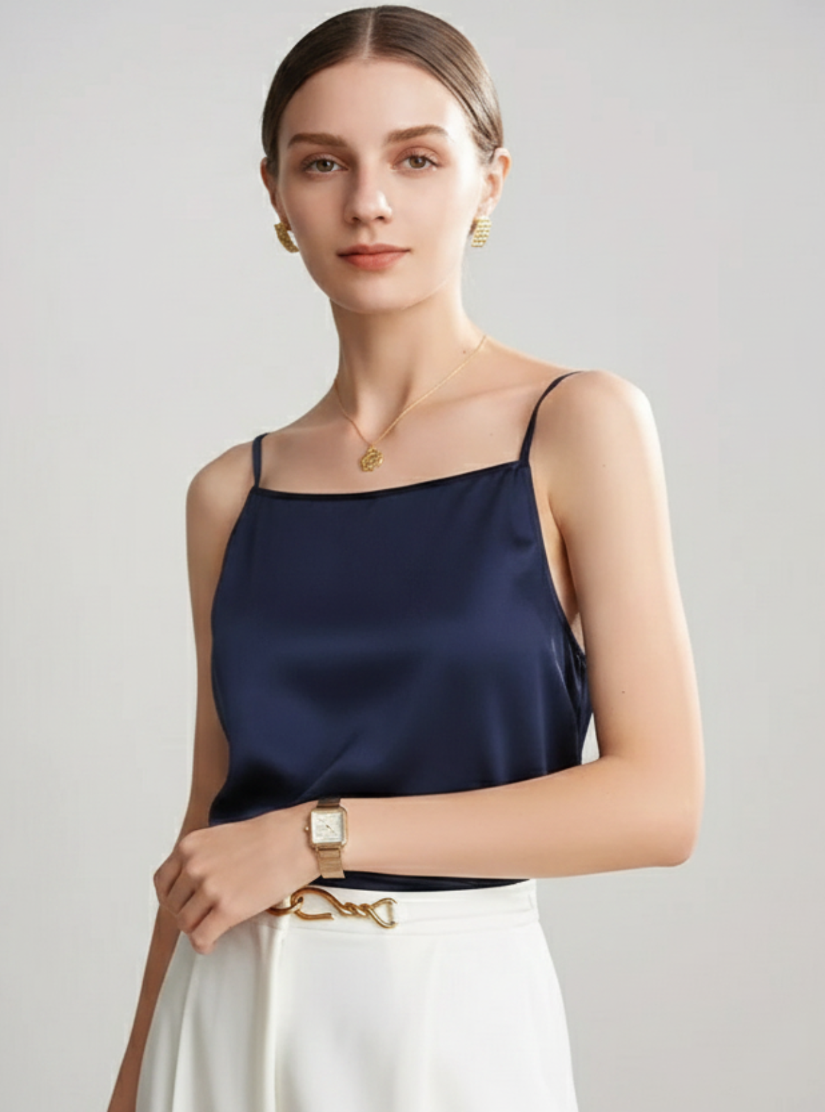 Woman wearing a navy satin top and white pants on a gray background
