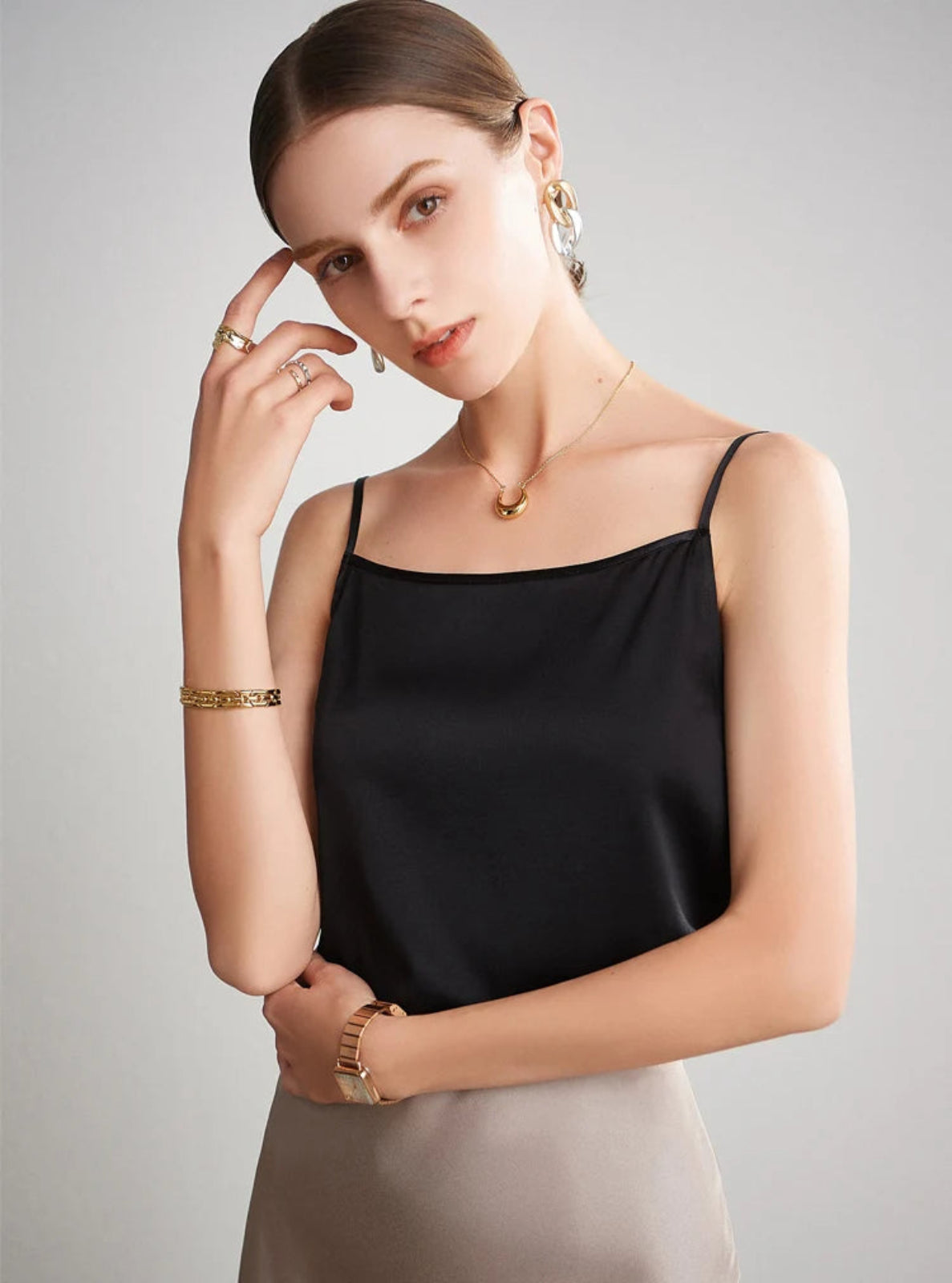 Woman wearing a black satin top with gold jewelry on a gray background