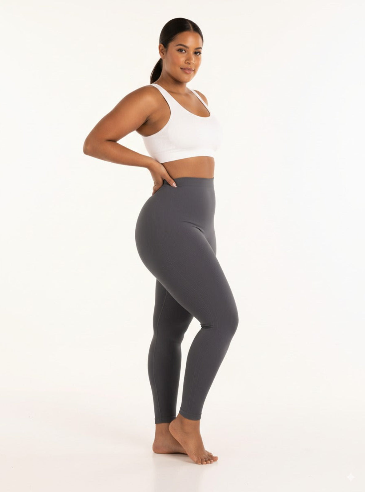 Woman wearing gray leggings and a white sports bra on a white background
