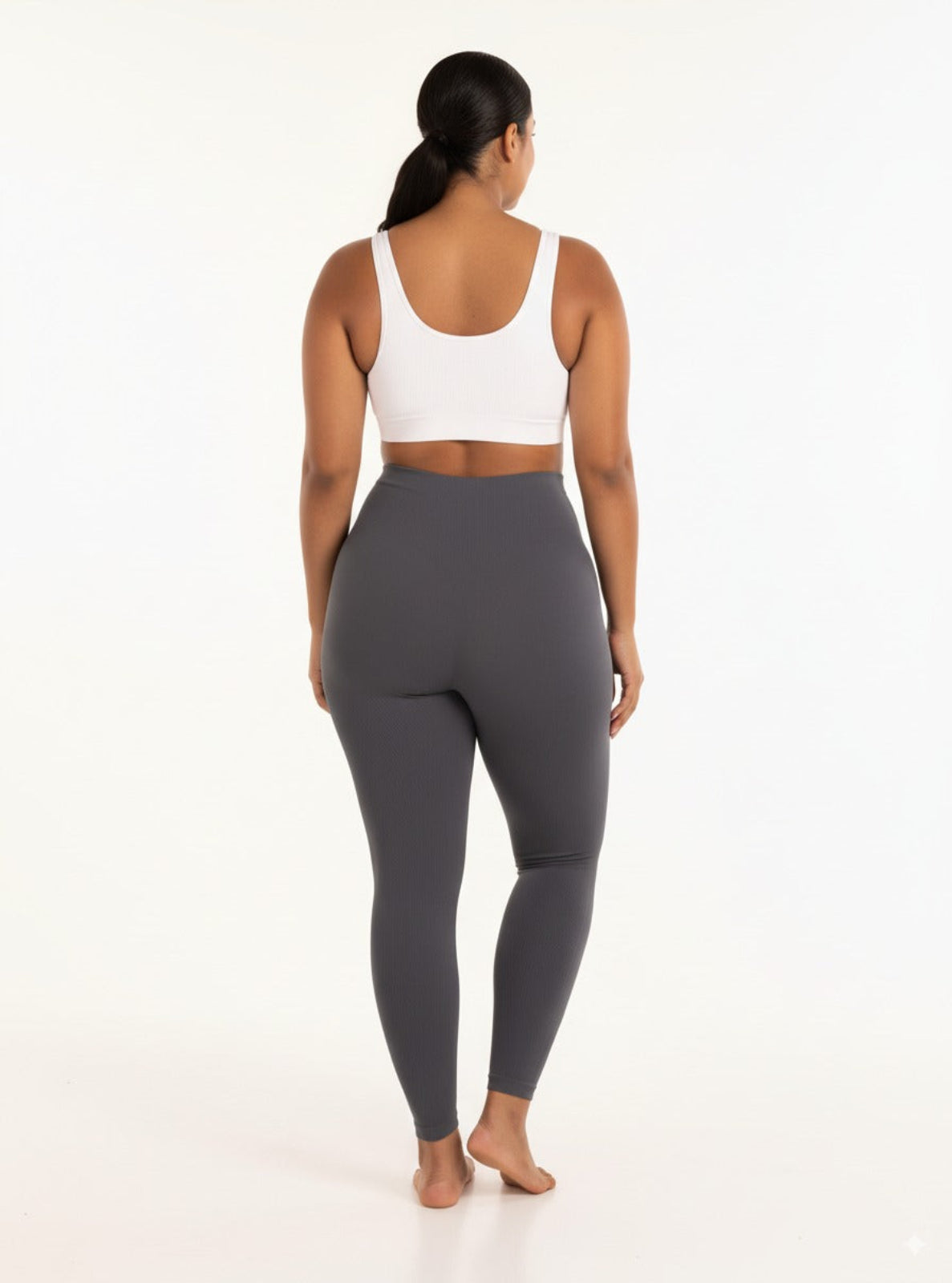 Person wearing gray leggings and a white sports bra on a white background