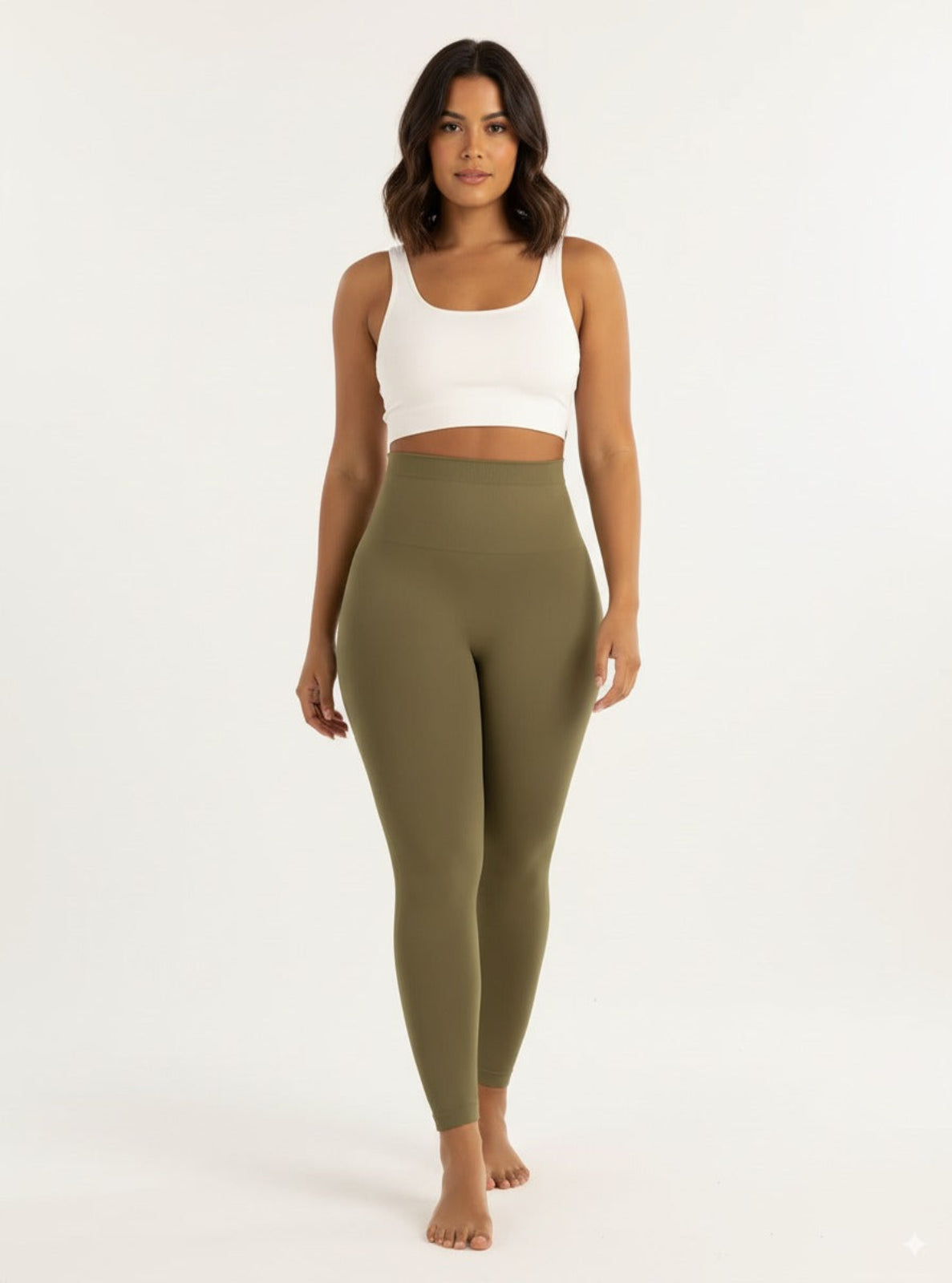 Woman wearing olive green leggings and a white sports bra on a white background