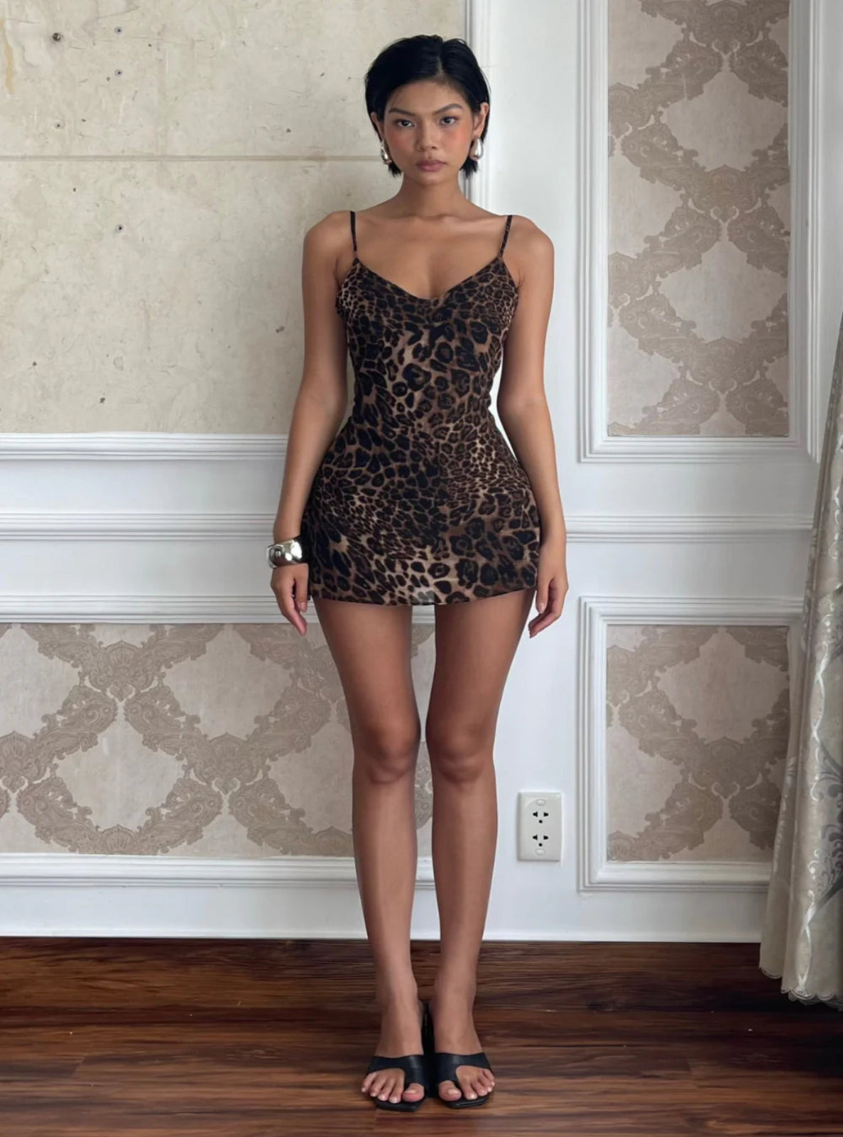 Woman wearing a leopard print dress standing in a room with patterned wallpaper.