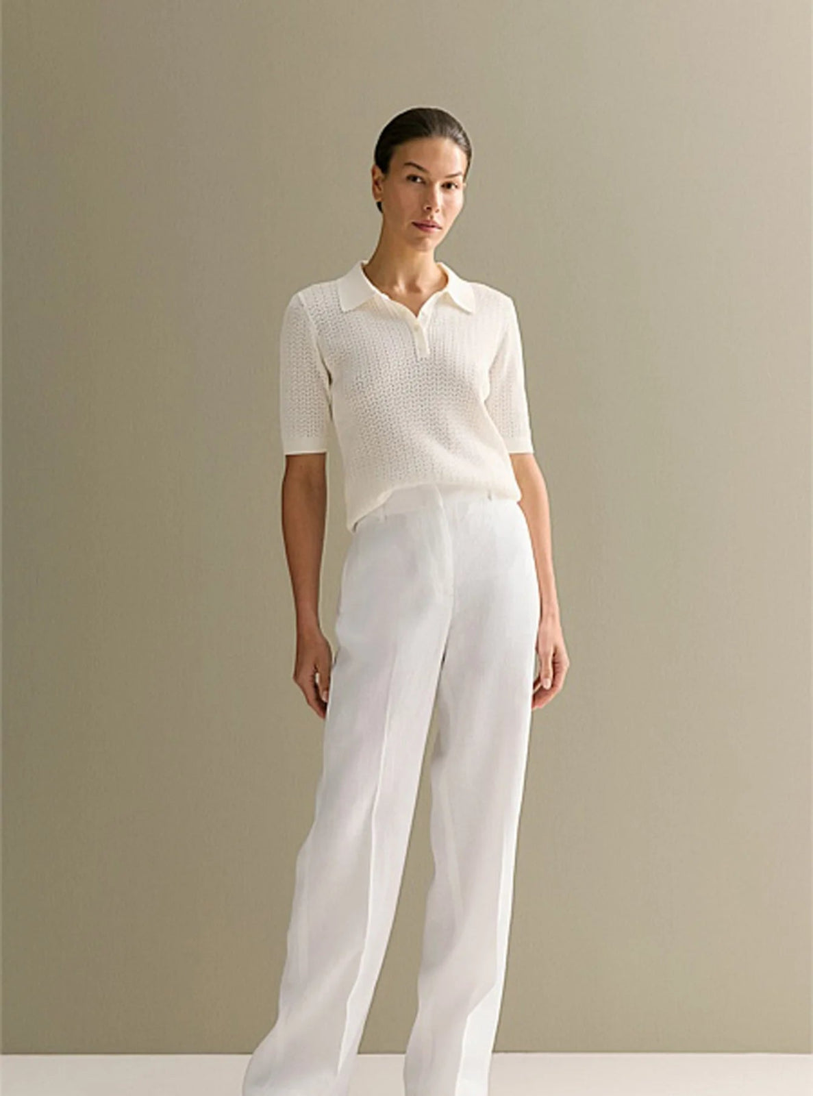 Woman wearing a white blouse and pants against a plain background