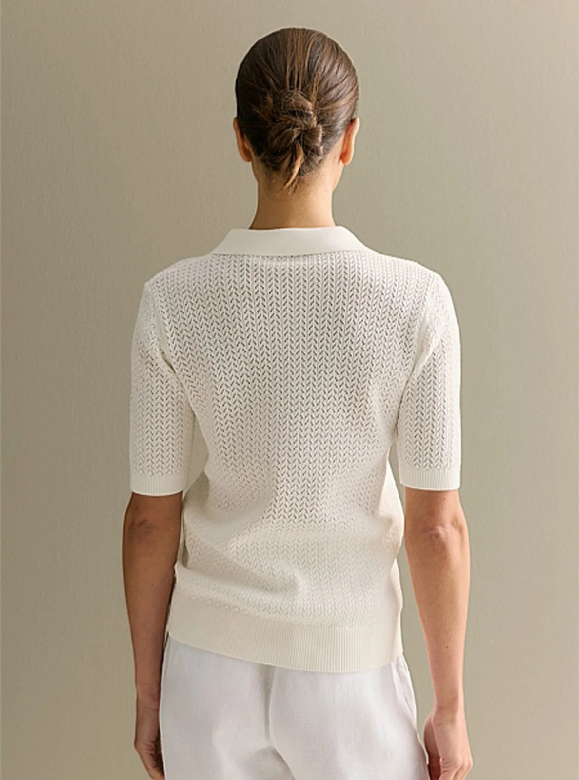 Person wearing a white knit cardigan against a beige background