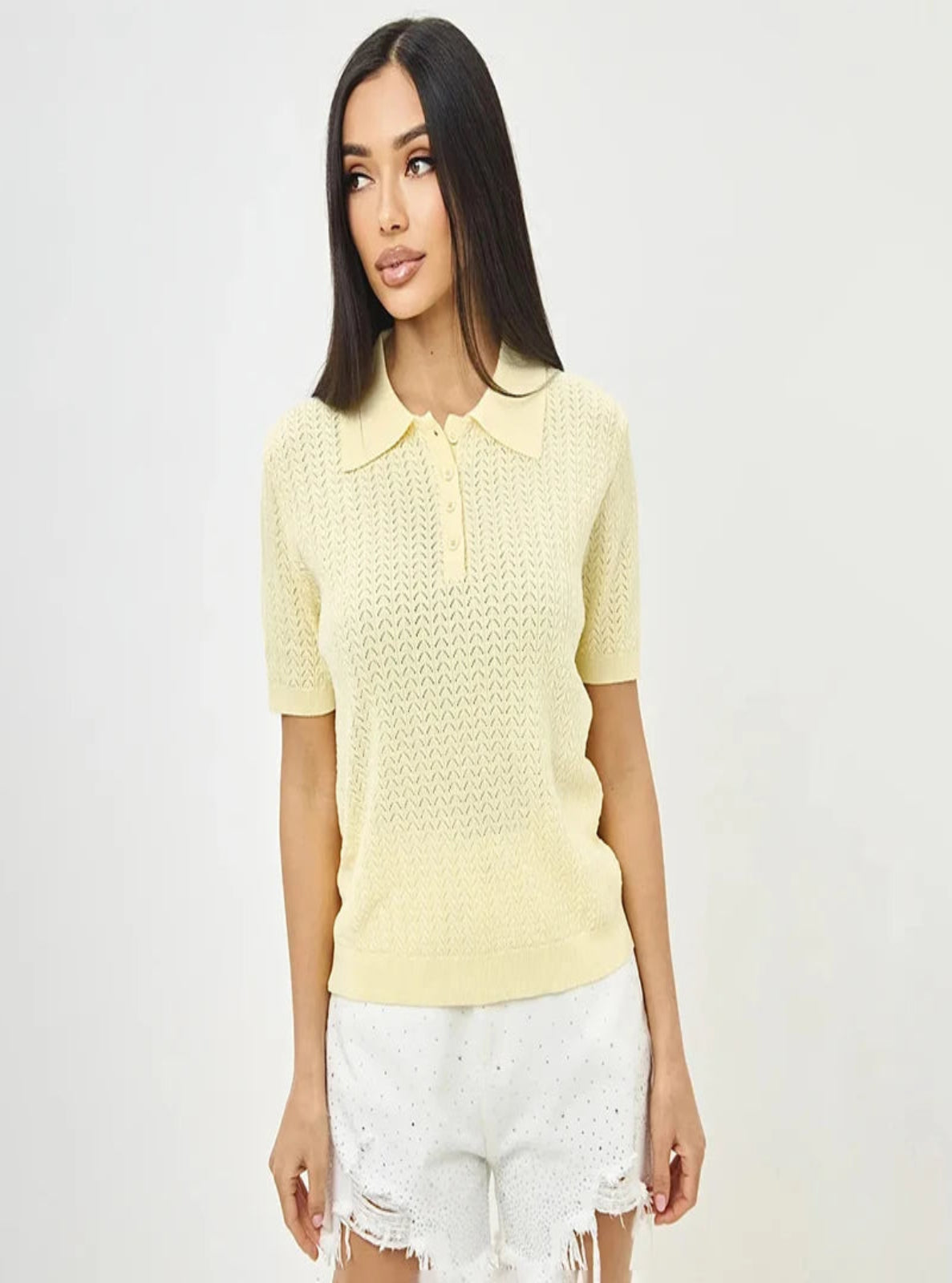 Woman wearing a light yellow knitted top with a plain background