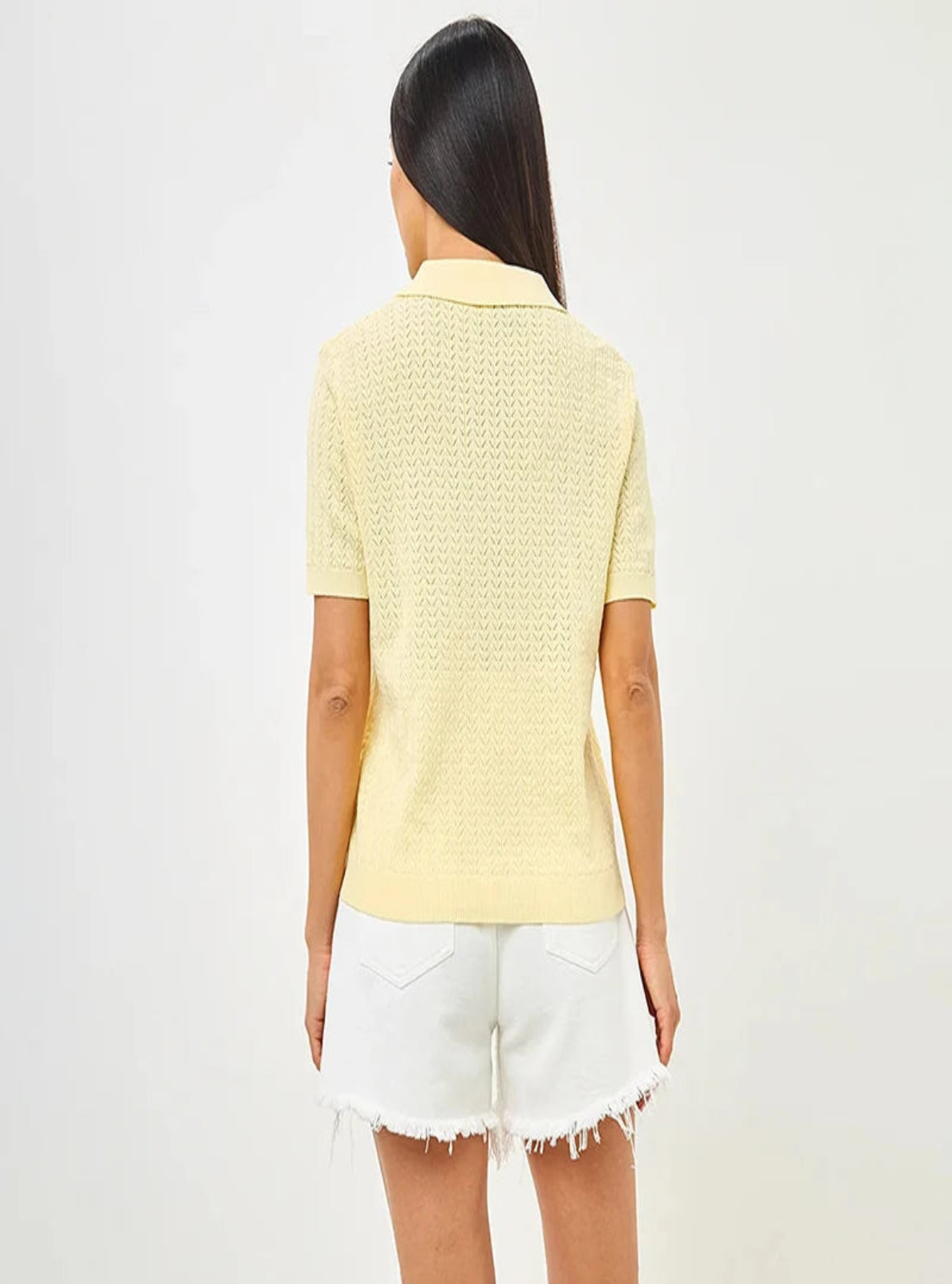 Person wearing a light yellow textured top and white shorts on a plain background