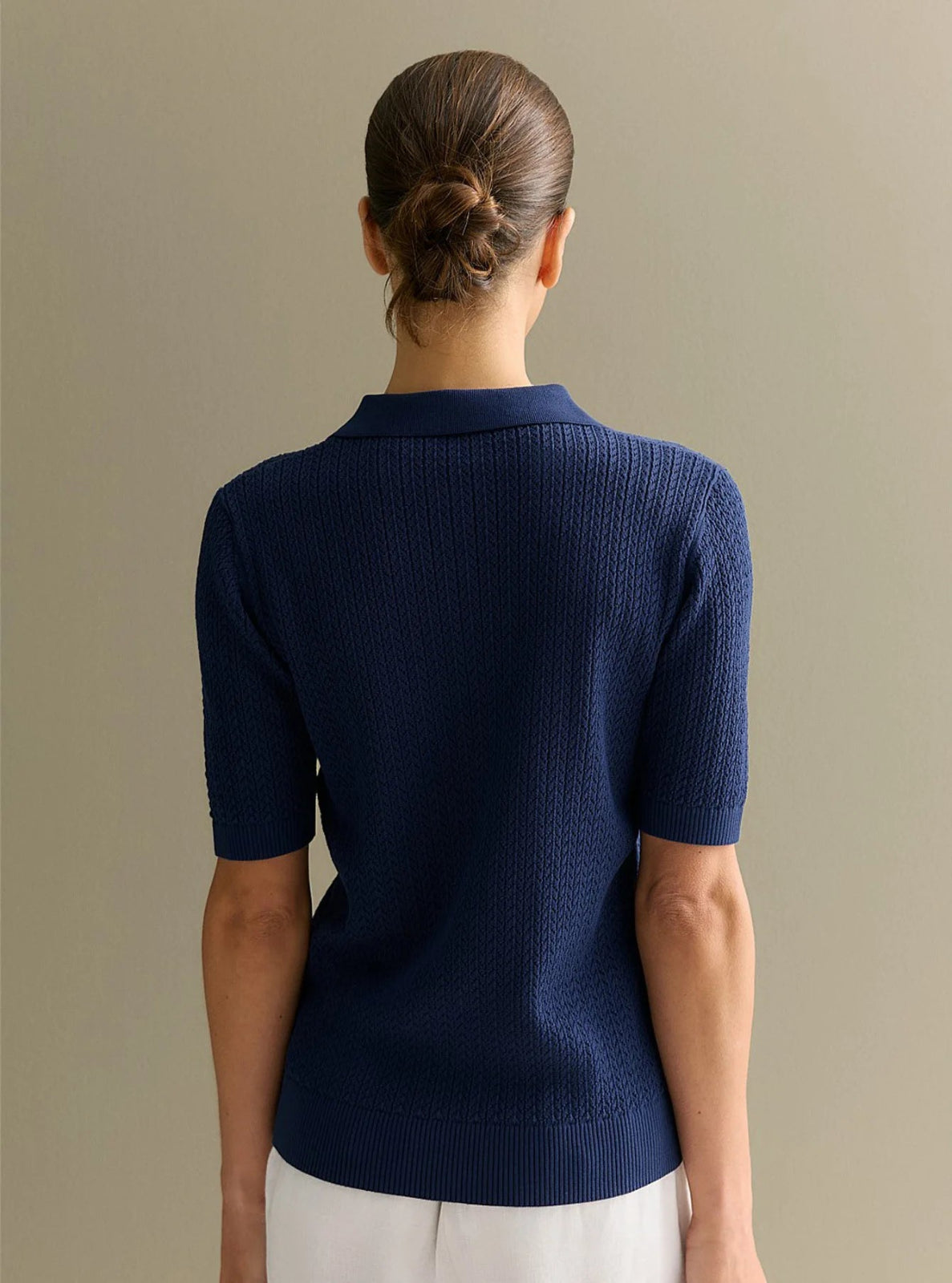 Person wearing a navy blue short-sleeve shirt against a beige background