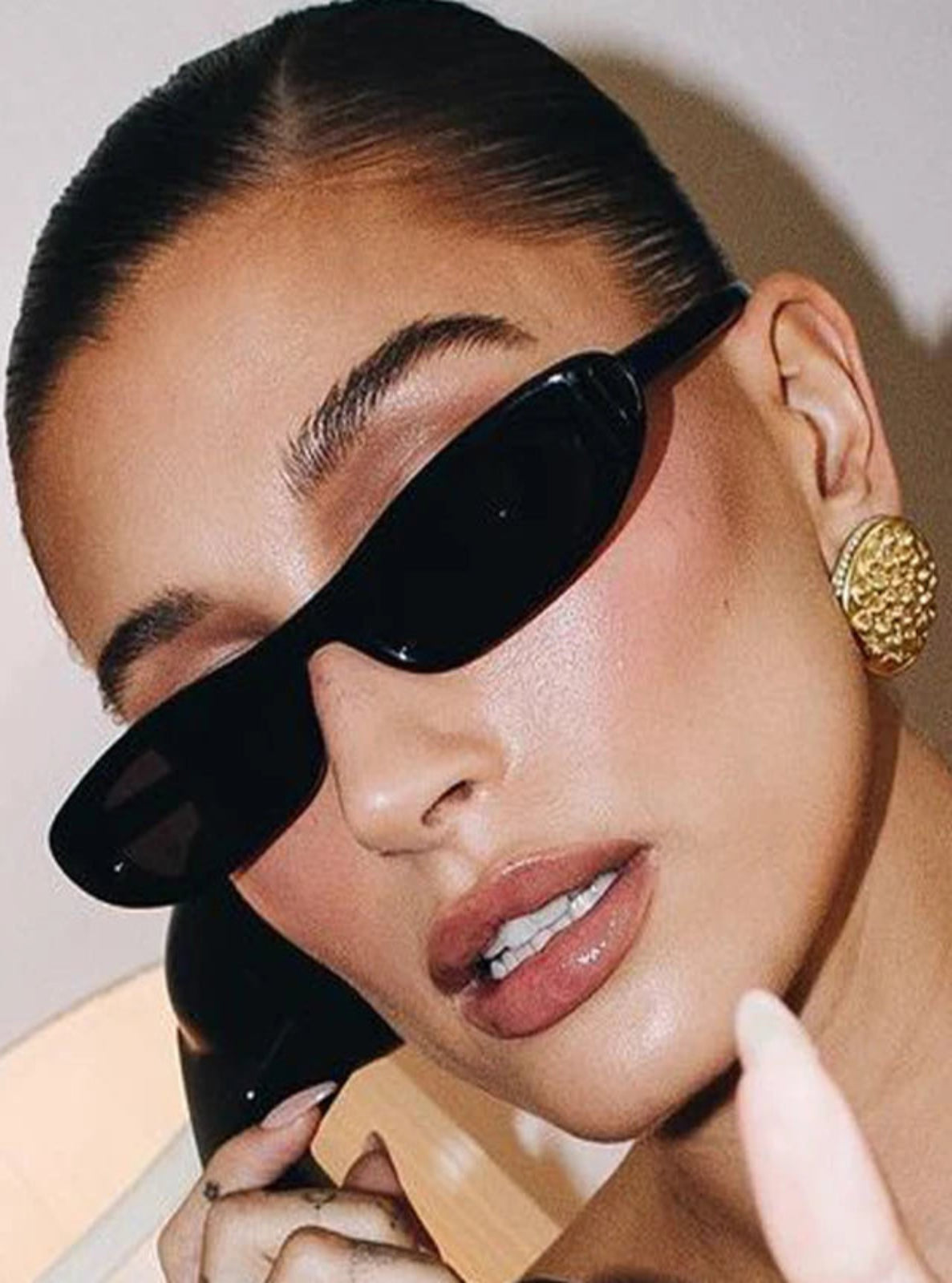 Close-up of a person wearing black sunglasses and a gold earring against a neutral background