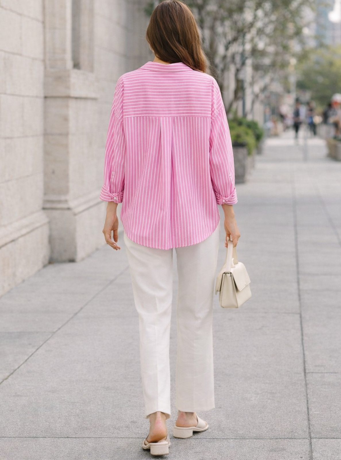 Person wearing a pink striped shirt and white pants walking on a city street.