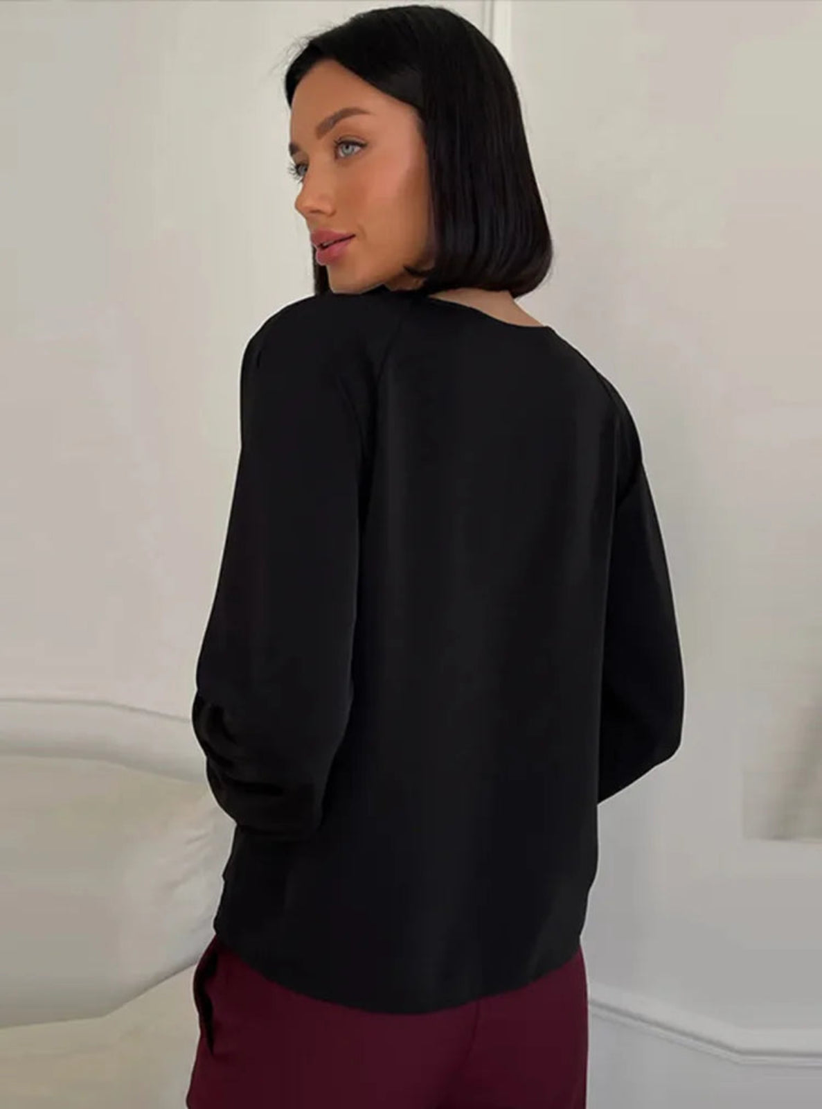 Person wearing a black blouse and burgundy pants against a white background