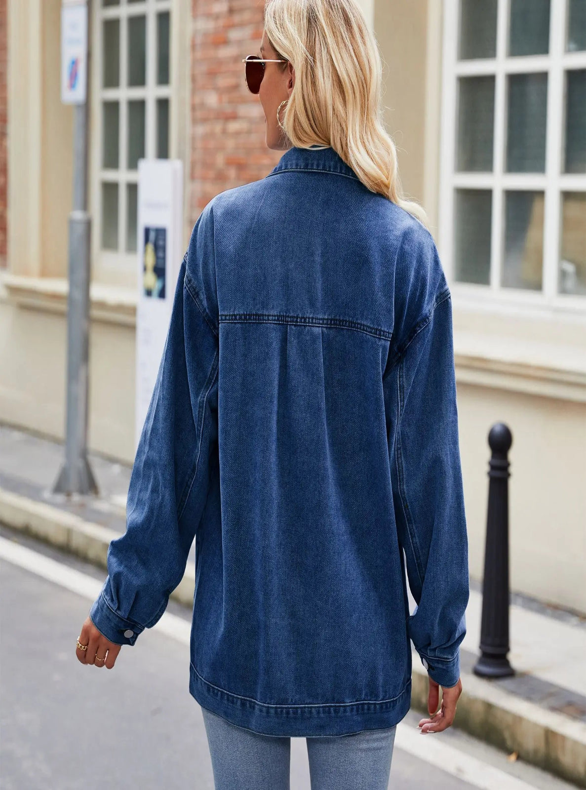 Woman wearing a blue denim jacket walking on a street.
