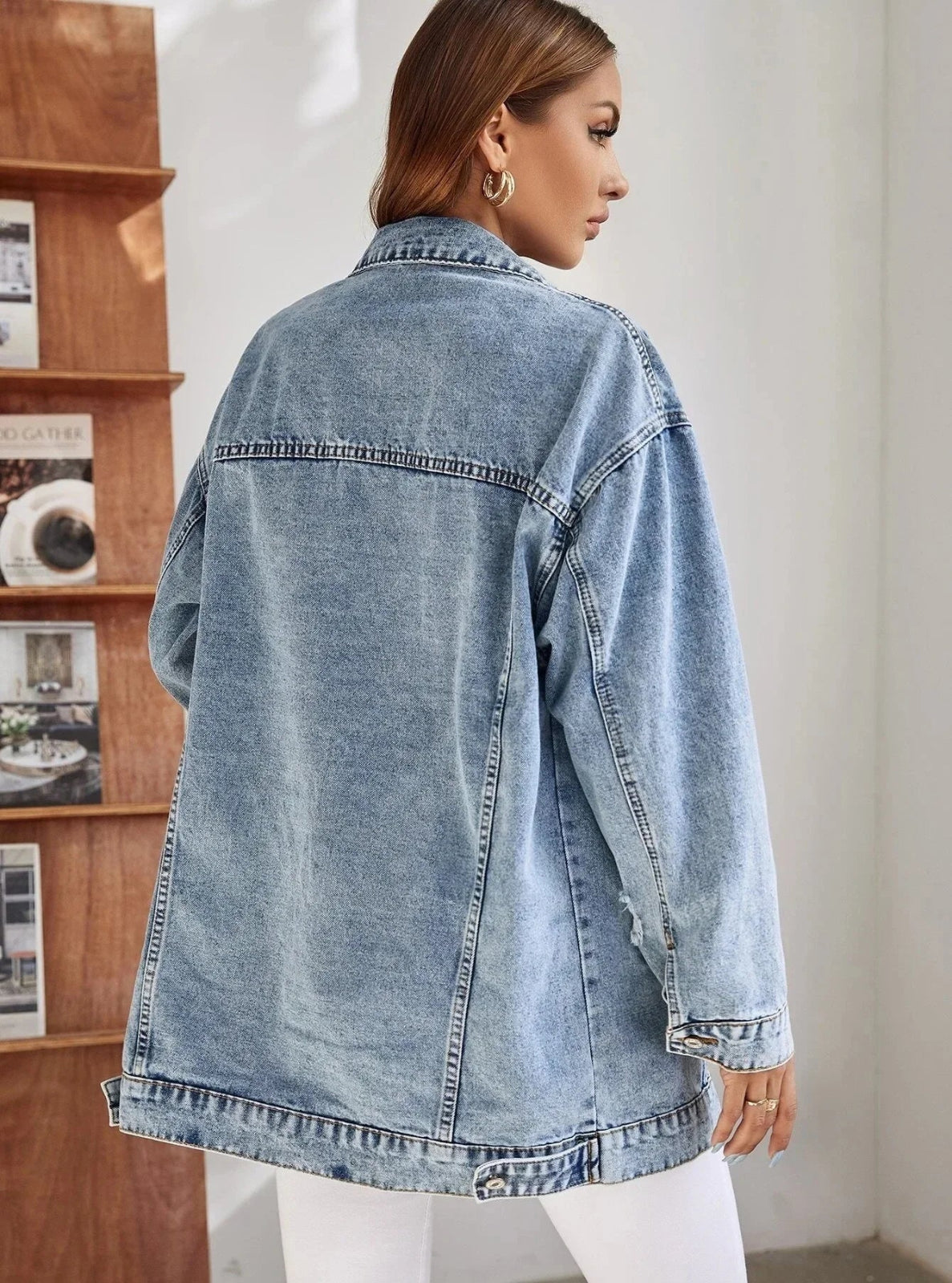 Person wearing a light blue denim jacket in a room with a bookshelf.