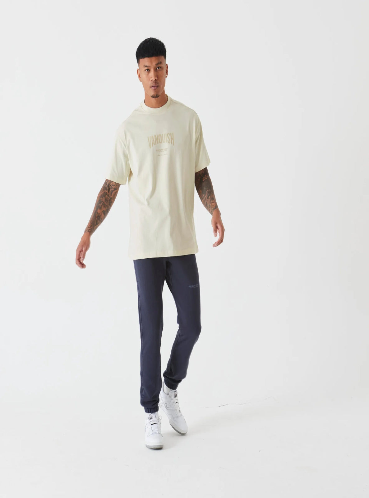 Man wearing a beige t-shirt and dark pants on a white background