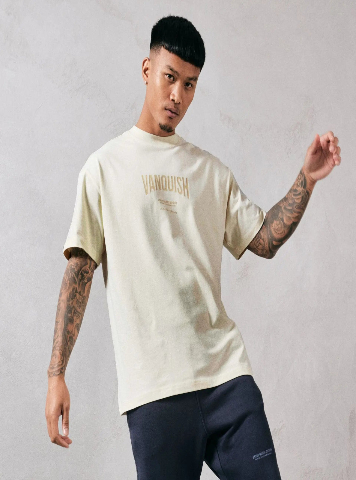 Man wearing a beige 'Vanquish' t-shirt against a gray background