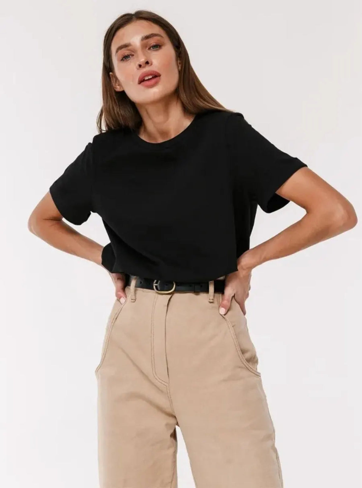 Woman wearing a black t-shirt and beige pants on a white background