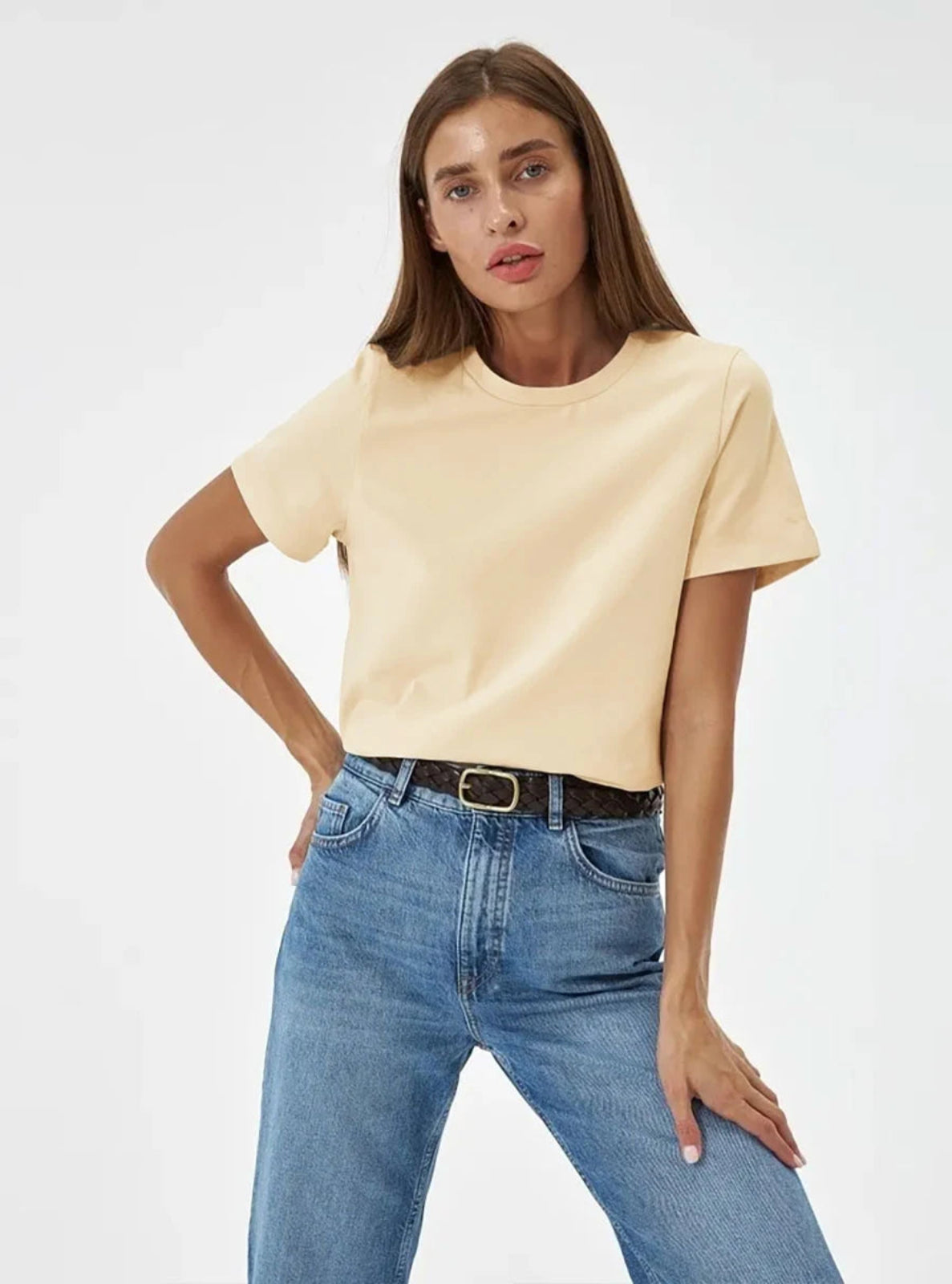 Woman wearing a beige t-shirt and blue jeans on a white background