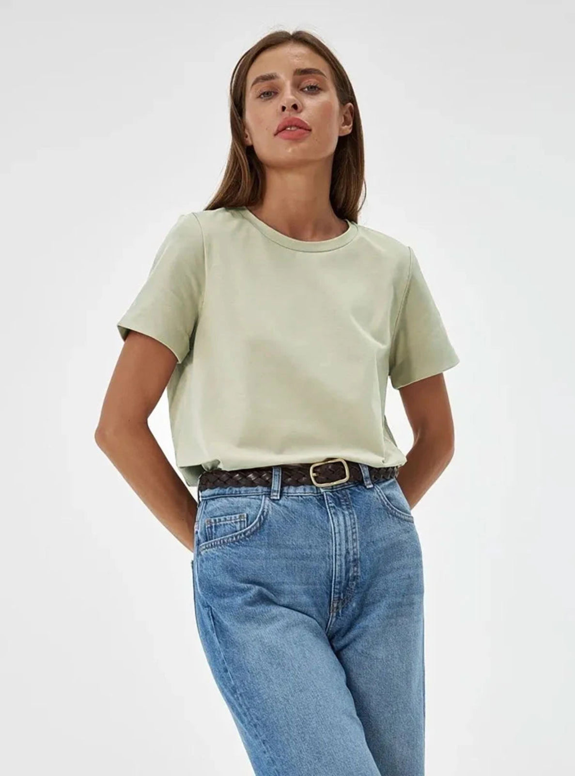 Woman wearing a light green t-shirt and blue jeans on a white background