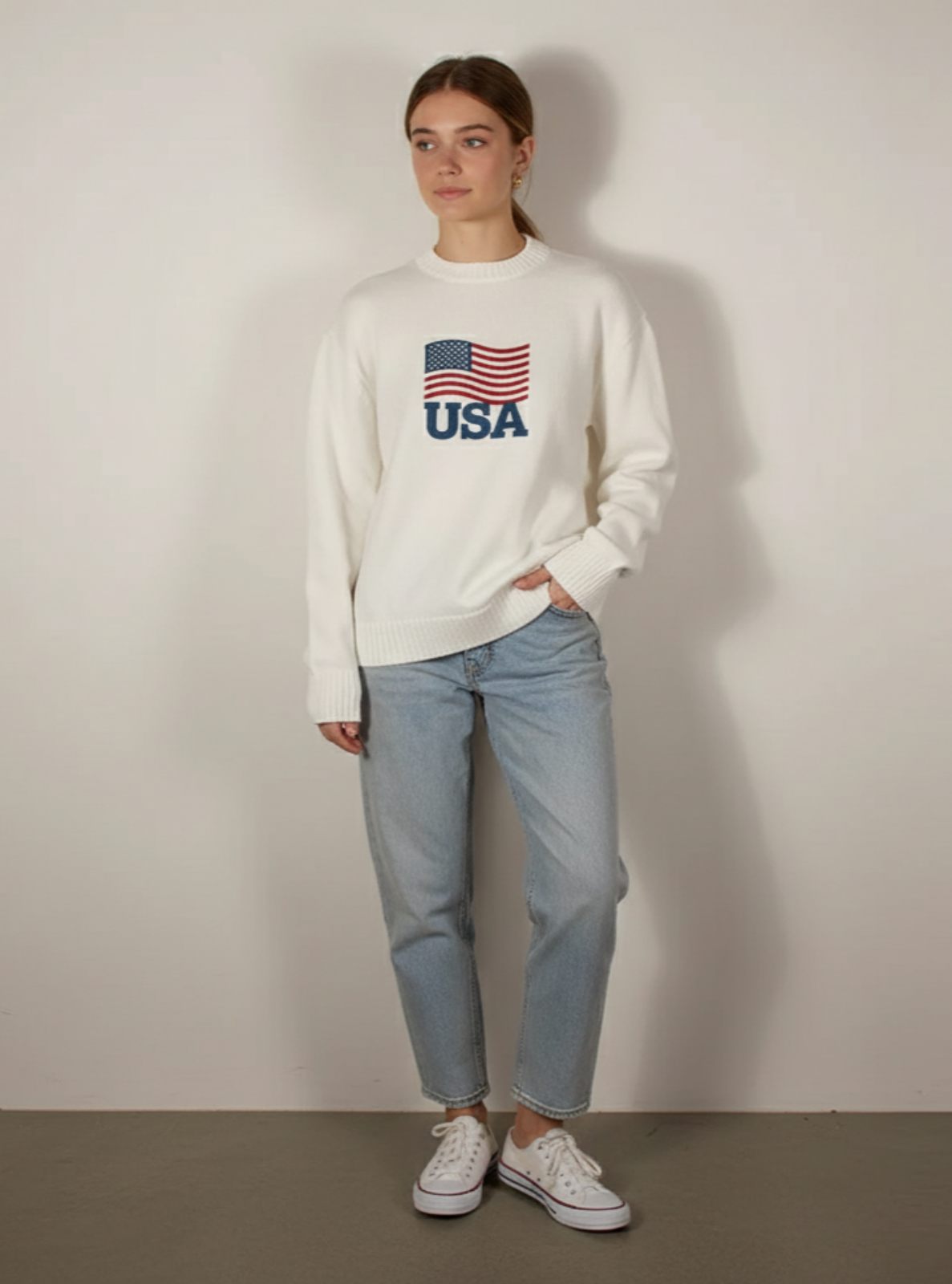 Person wearing a white sweatshirt with an American flag design and text, standing against a plain background.