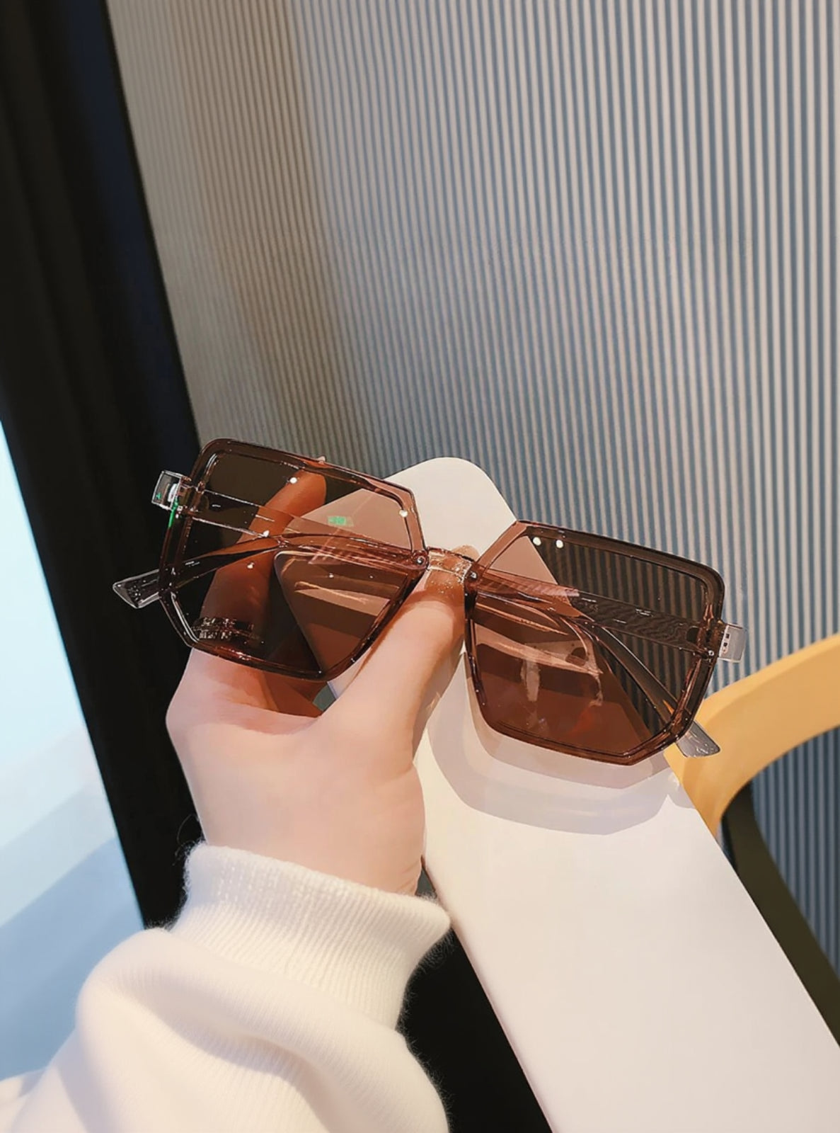 Brown sunglasses held by a hand with a blurred background