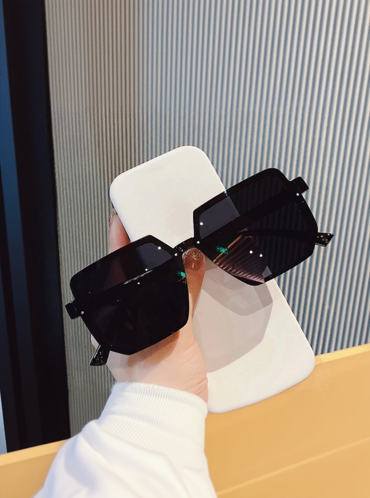 Black sunglasses held by a hand against a neutral background
