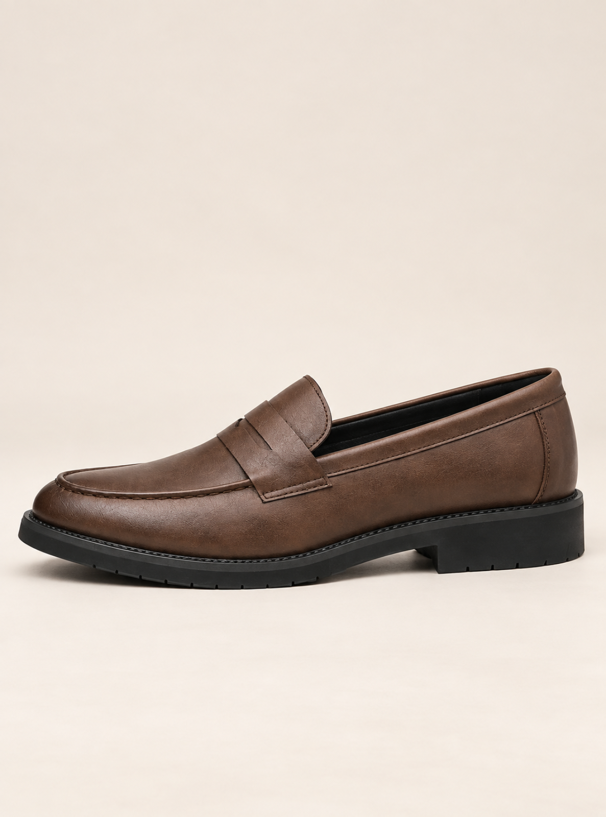 A single brown leather penny loafer with a black sole, shown in a side profile against a light beige background.
