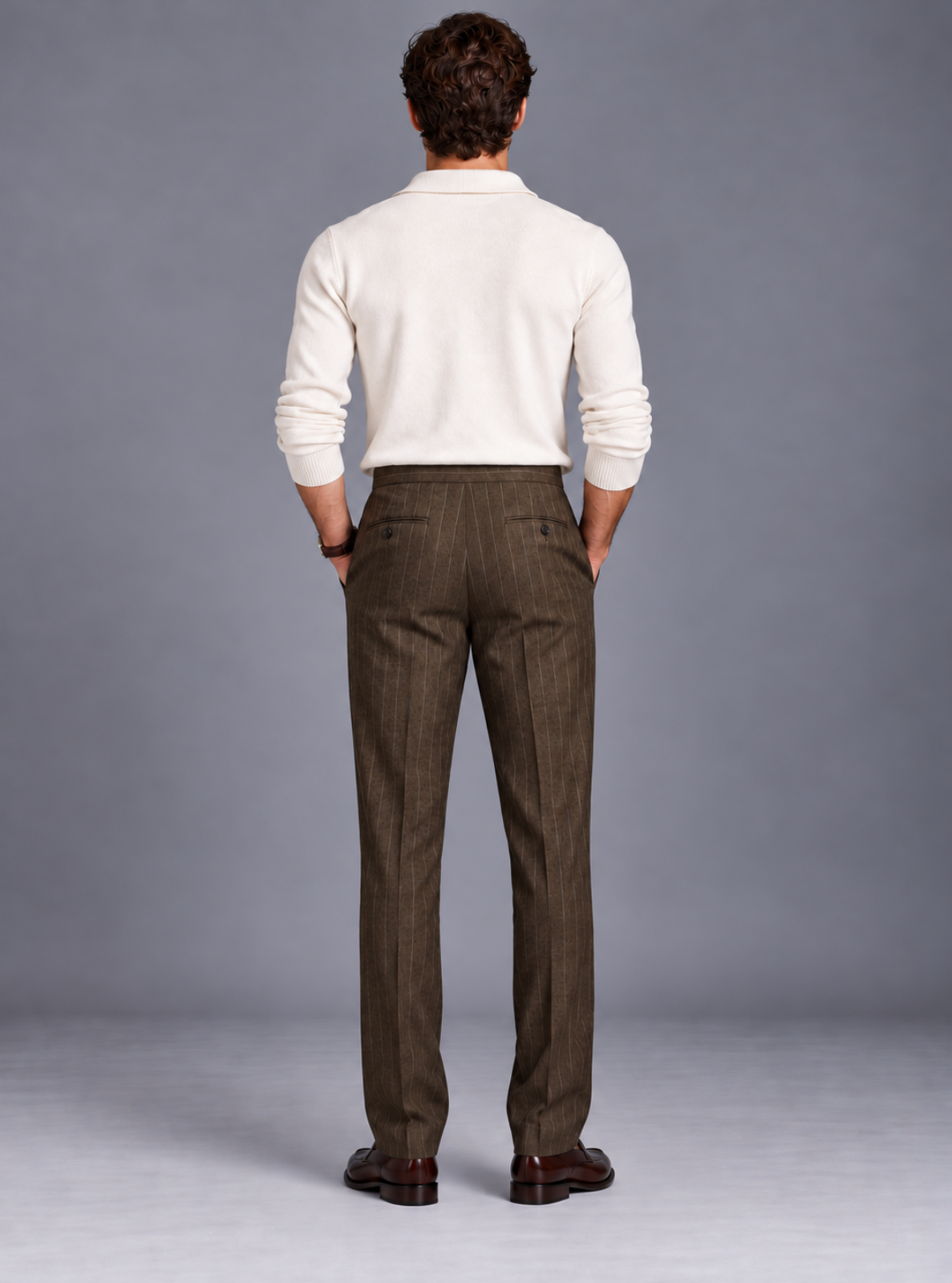 A man viewed from behind wearing a cream long-sleeve knit polo shirt and brown pinstriped trousers, standing against a neutral gray studio background.