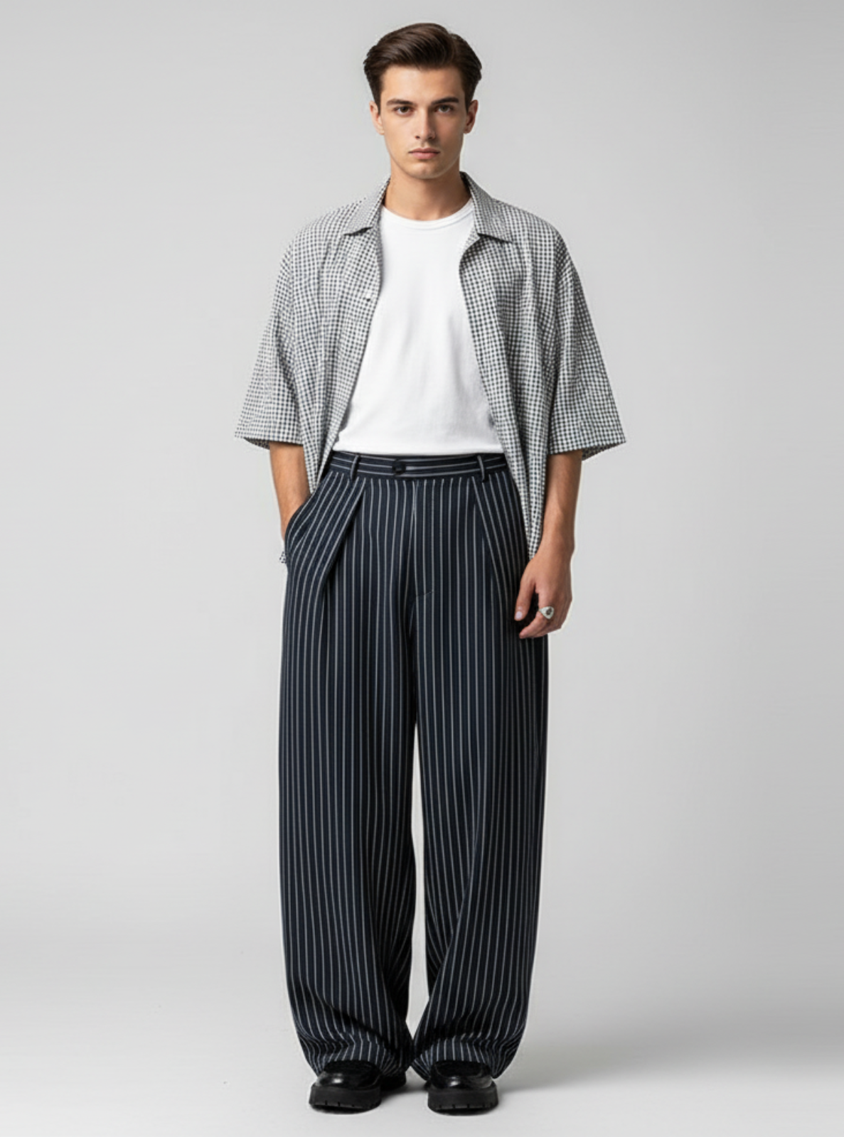 Man wearing a checkered shirt, white t-shirt, and striped pants on a gray background