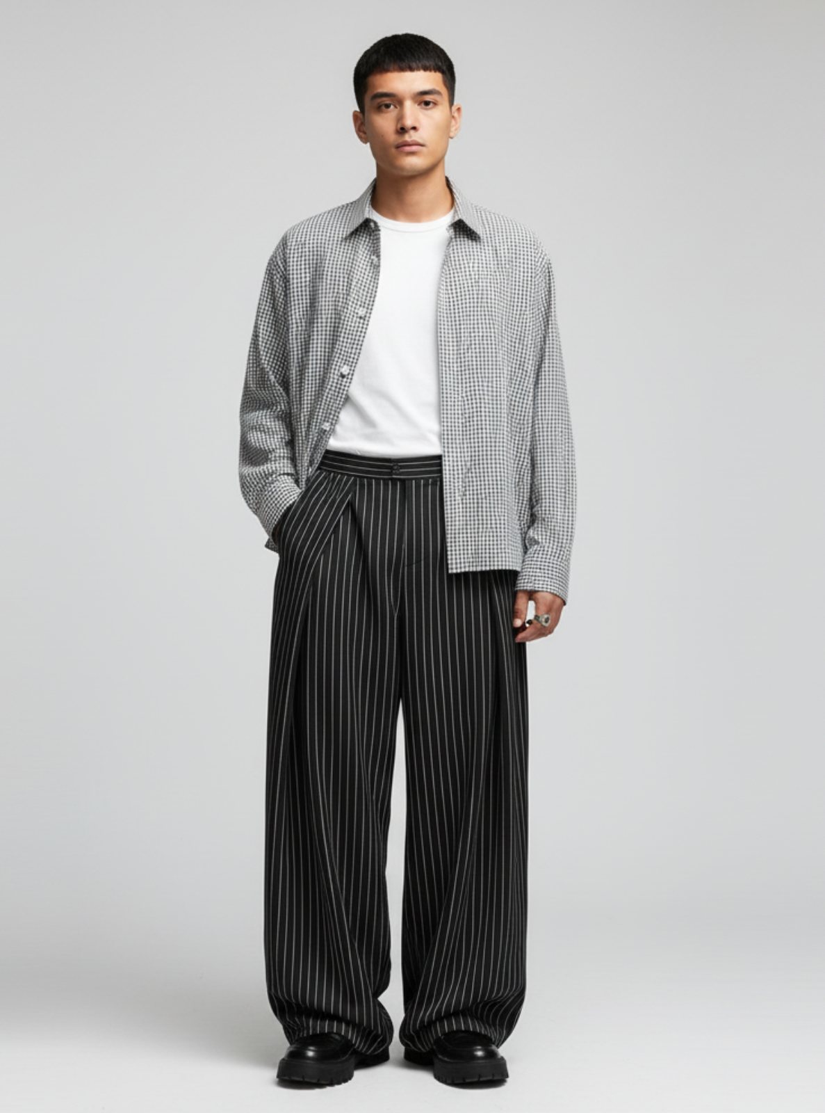 Man wearing a checkered shirt, white t-shirt, and black striped pants on a gray background