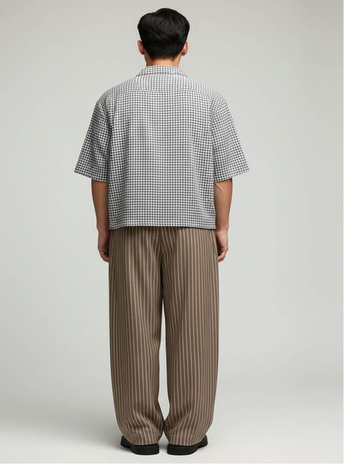 Person wearing a checkered shirt and striped pants on a plain background